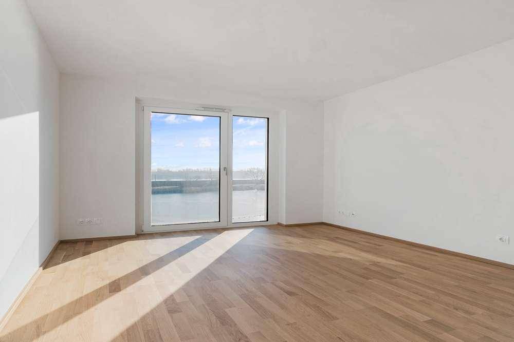 Helles Zimmer mit Parkettboden und großen Fenstern, die den Raum mit Tageslicht füllen.