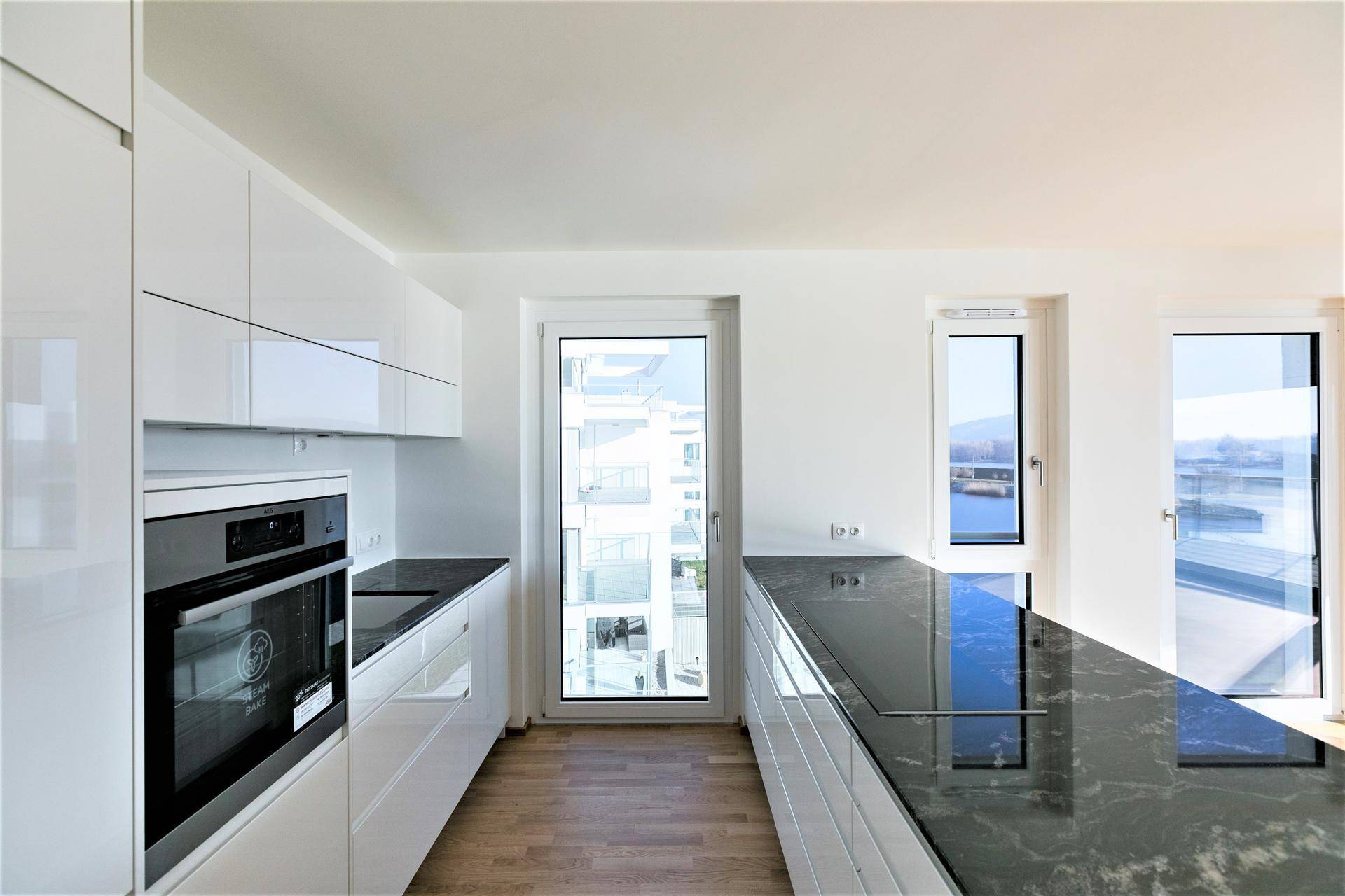 Moderne Küche mit weißen Hochglanzfronten, dunkler Arbeitsplatte und Blick auf den Fluss.