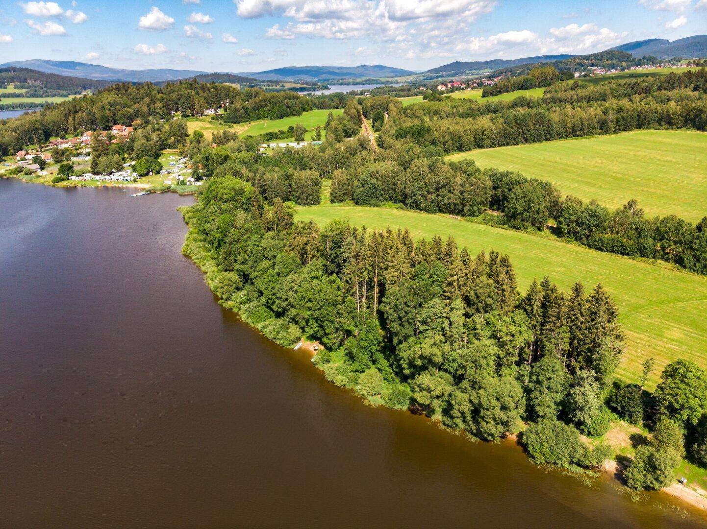 Luftaufnahme einer malerischen Seenlandschaft, umgeben von dichten Wäldern und grünen Feldern.