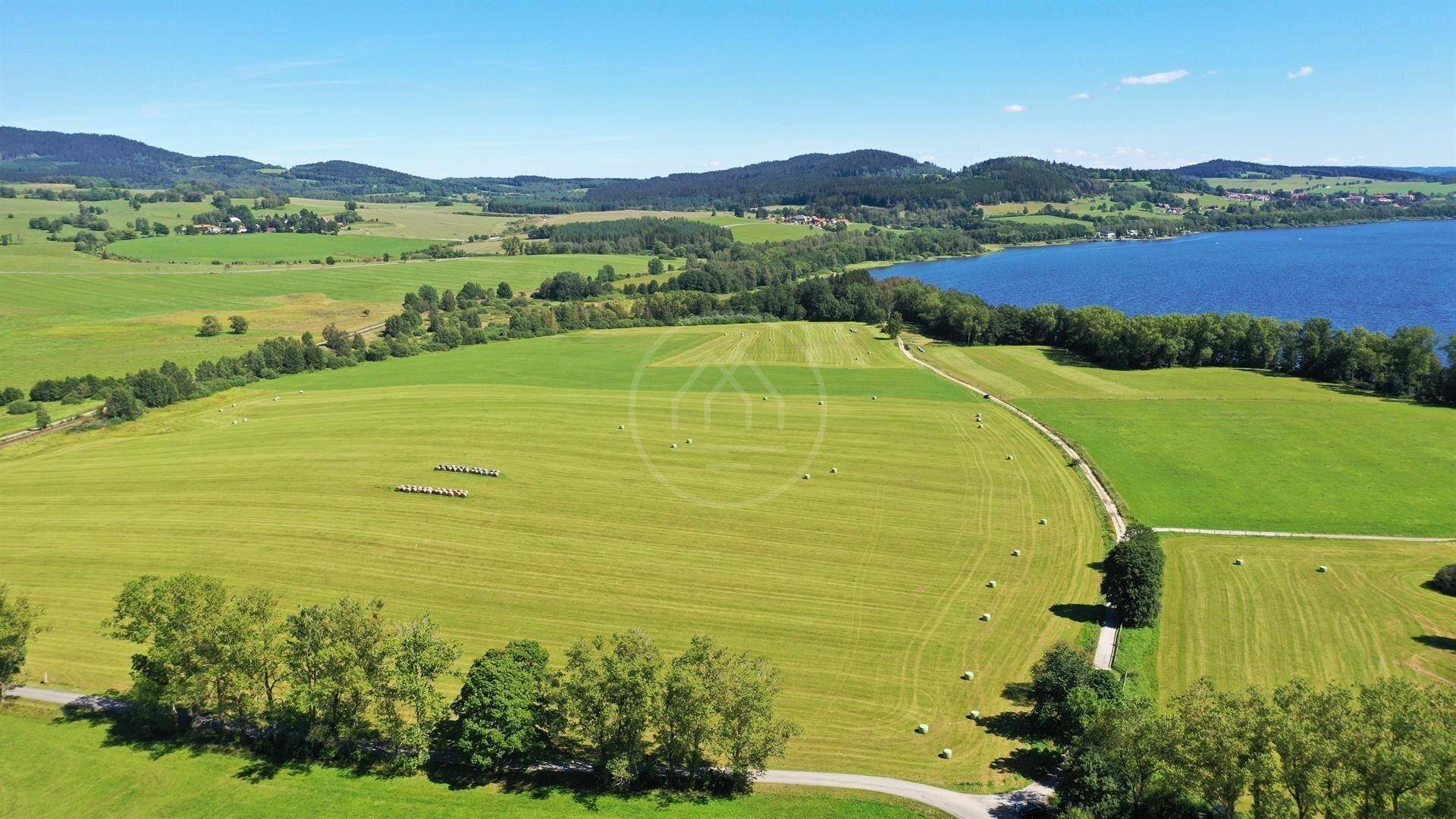 Weitläufige Luftaufnahme einer ländlichen Gegend mit grünen Feldern, einem See und einer Straße im Vordergrund.