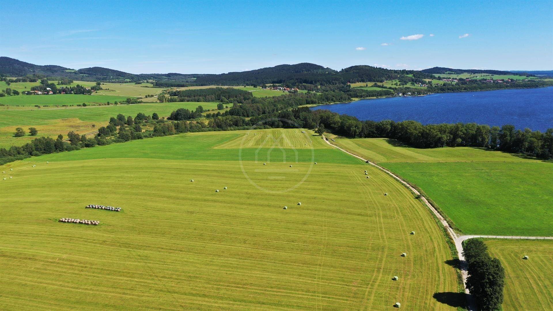 Panoramische Luftaufnahme einer idyllischen Landschaft mit weiten Feldern, einem blauen See und bewaldeten Bergen.