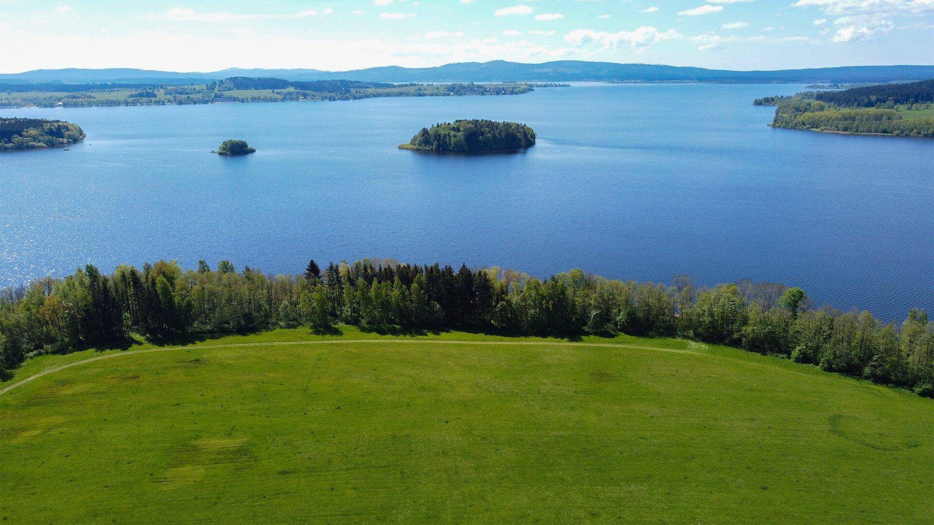 Weitläufige Landschaft mit einem großen See, kleinen Inseln, grünen Feldern und Wäldern.