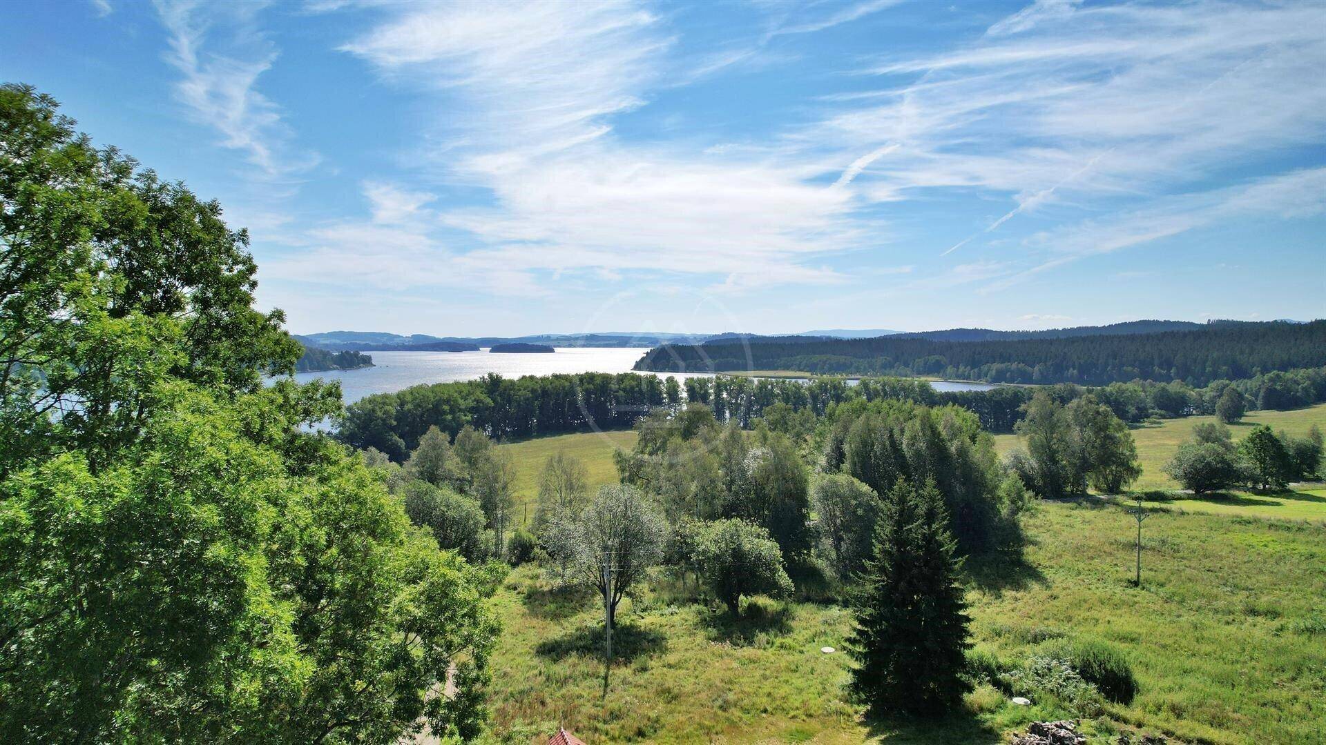 Panoramablick über einen weiten See, umgeben von üppigen Wäldern und grünen Landschaften unter einem bewölkten Himmel.