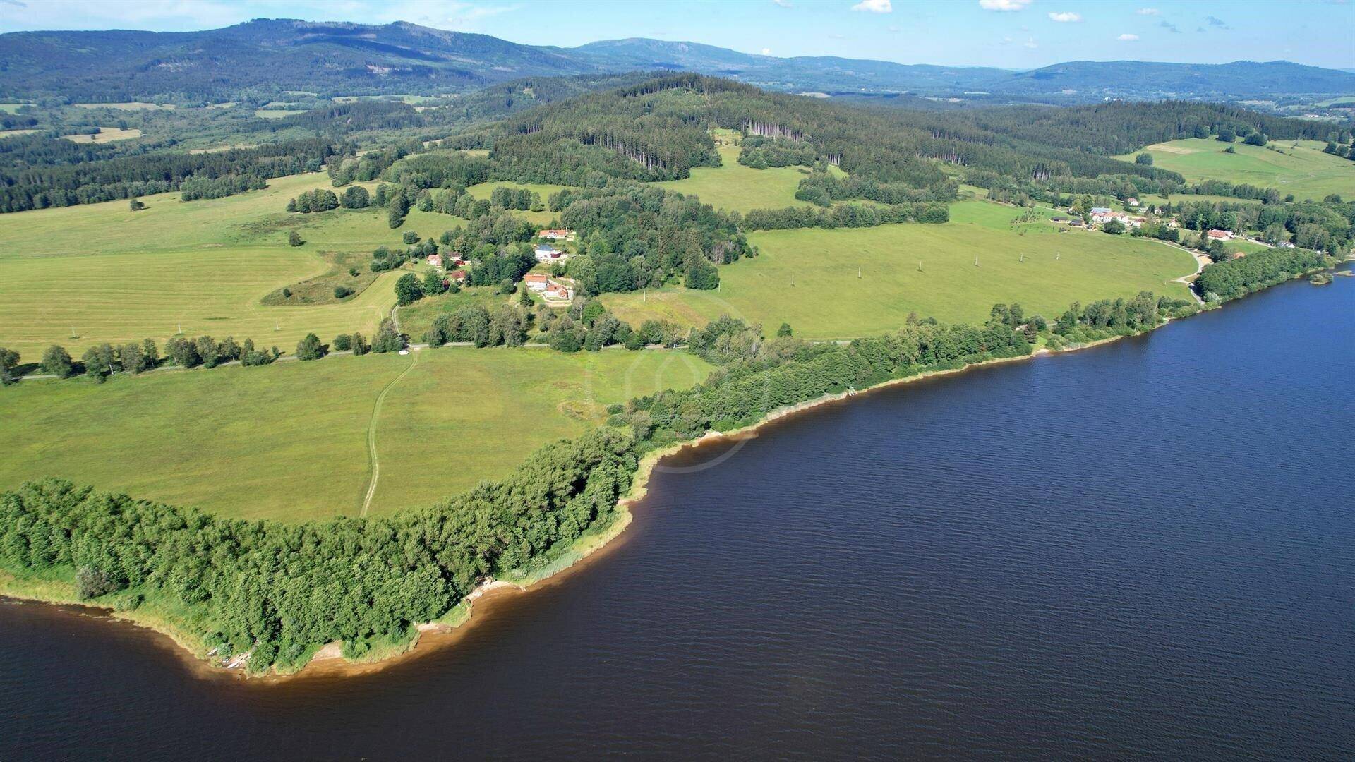 Luftaufnahme der Seenlandschaft mit grünen Feldern, Wäldern und vereinzelten Gebäuden am Ufer.