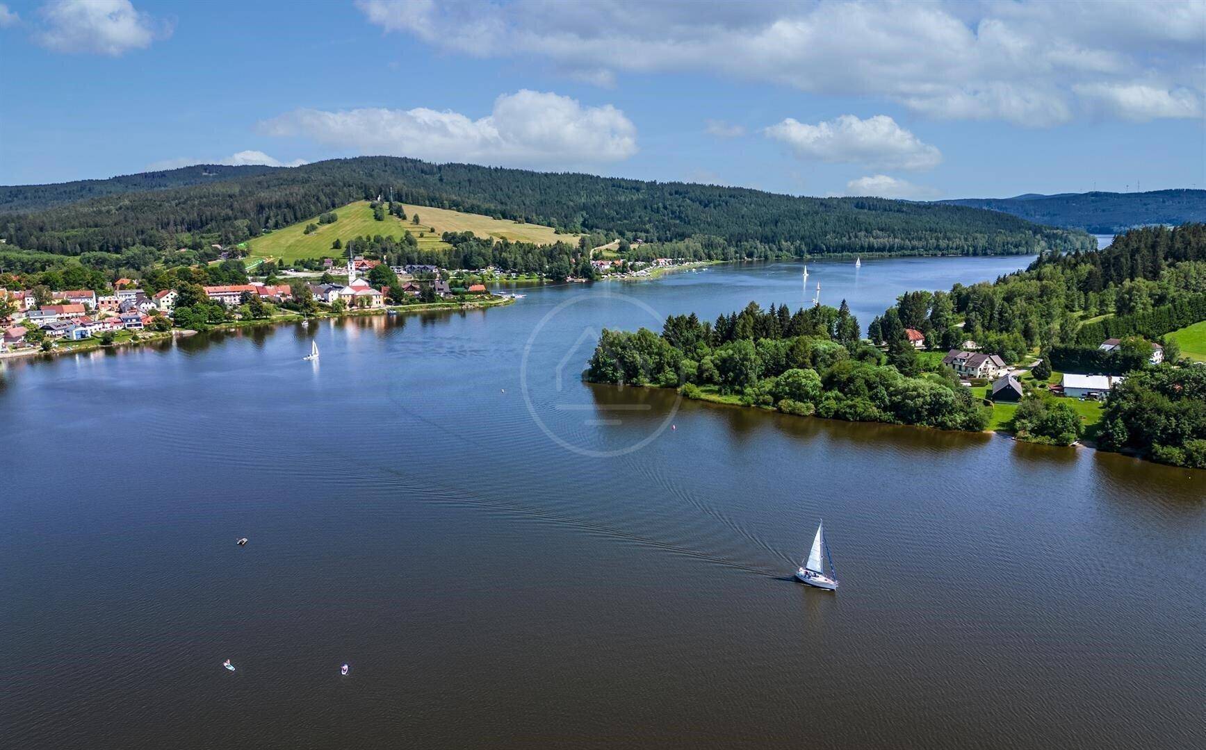 Panoramablick aus der Vogelperspektive auf einen großen See mit Segelbooten, umgeben von Wäldern und einem Dorf.