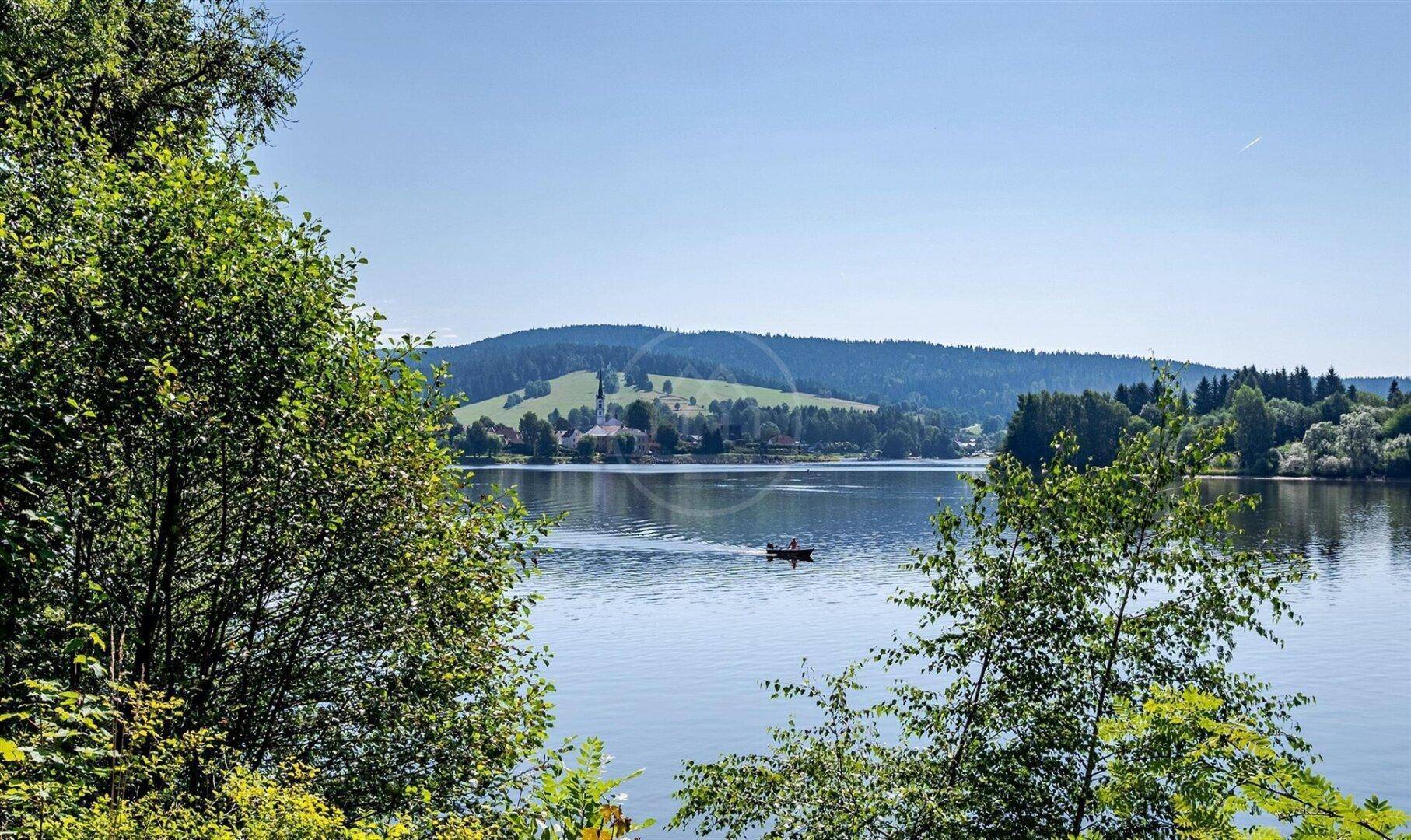 Malerischer Blick auf den See, umrahmt von Bäumen, mit einem Boot in der Ferne und bewaldeten Hügeln.