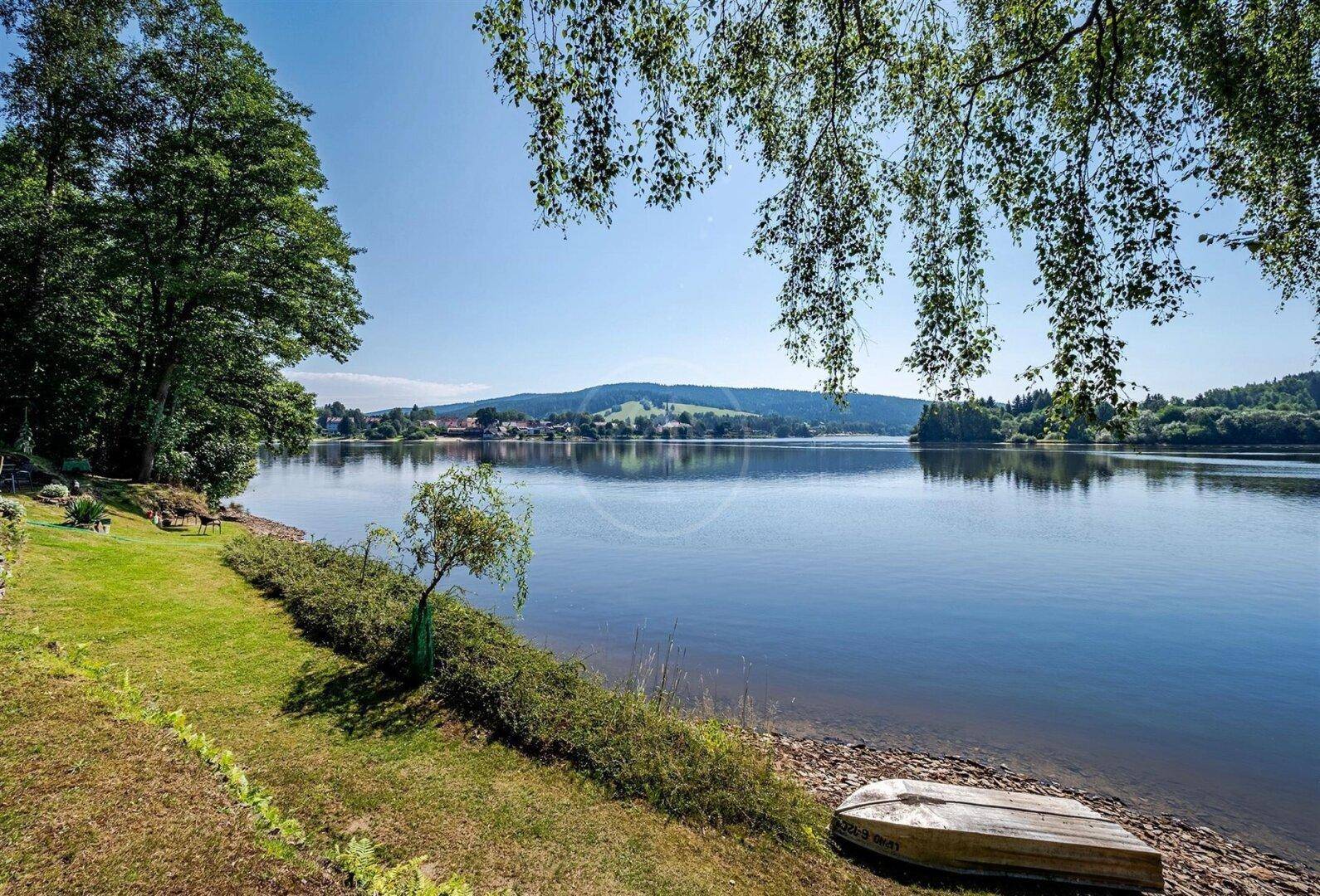 Panoramablick auf den See von einer grünen Uferböschung mit einem kleinen Boot am sandigen Strand.