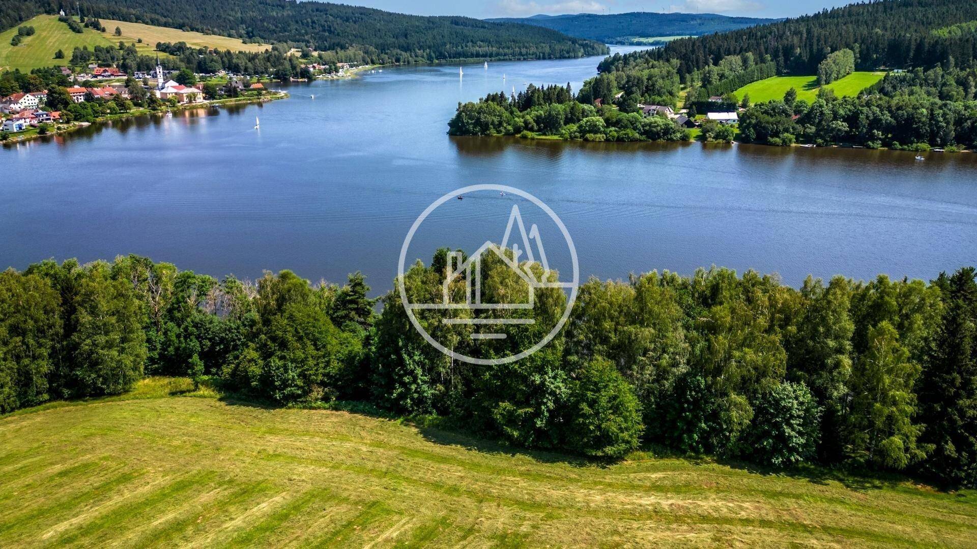 Panoramablick auf einen weitläufigen See mit Segelbooten, umgeben von Wäldern und einer kleinen Ortschaft.
