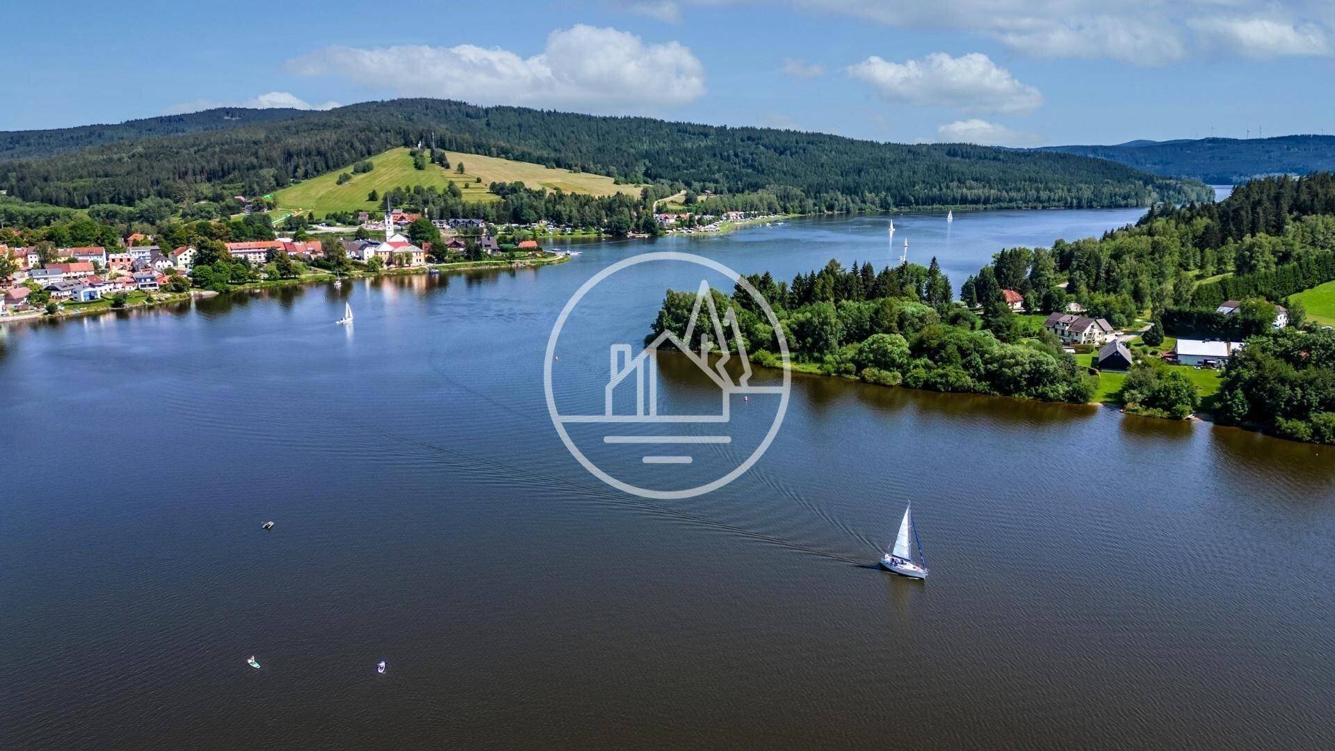Luftaufnahme eines großen Sees mit Segelbooten, umgeben von grünen Wäldern und einer charmanten Ortschaft.