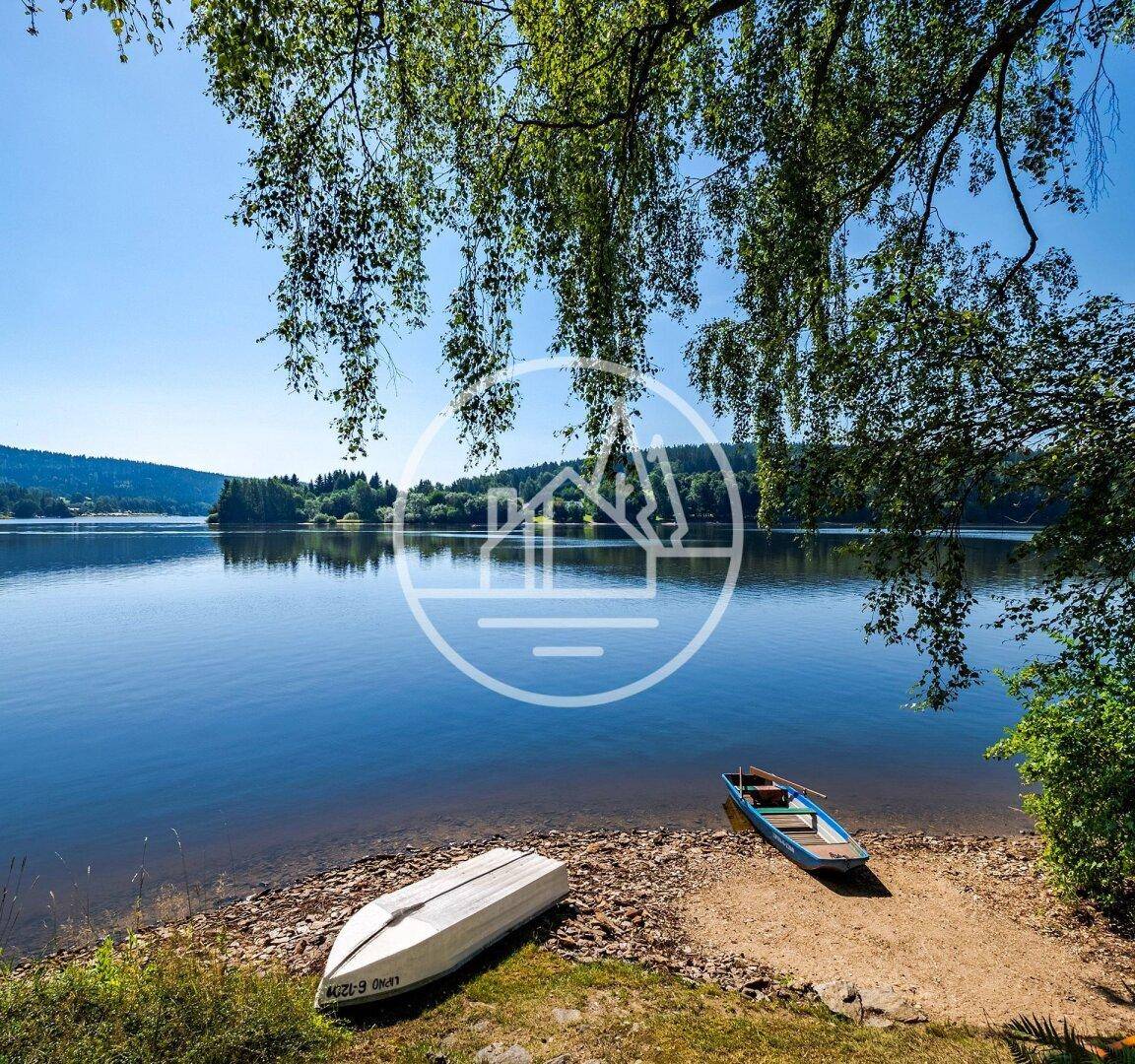 Idyllisches Seeufer mit zwei kleinen Booten am sandigen Strand, umgeben von grünen Bäumen.