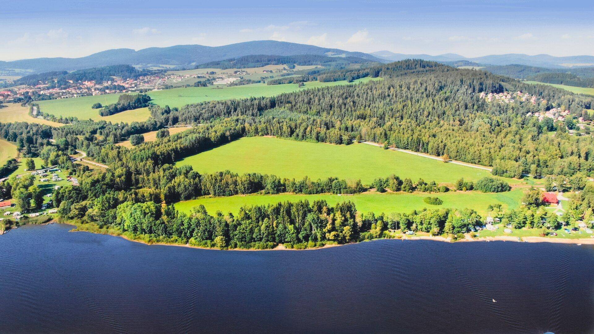 Malerische Luftaufnahme einer Seenlandschaft mit Wäldern, Feldern und sanften Hügeln im Hintergrund.