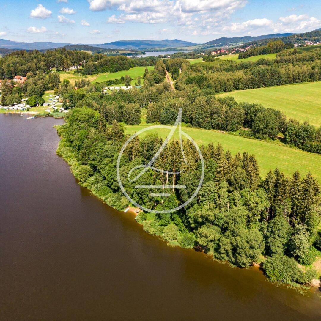 Panoramablick aus der Vogelperspektive auf einen See, umgeben von dichten Wäldern und Wiesen.