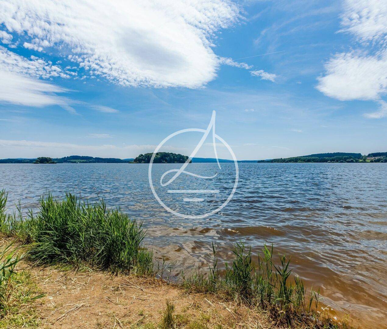 Weitläufiger See mit einer kleinen Insel im Hintergrund unter einem blauen Himmel.