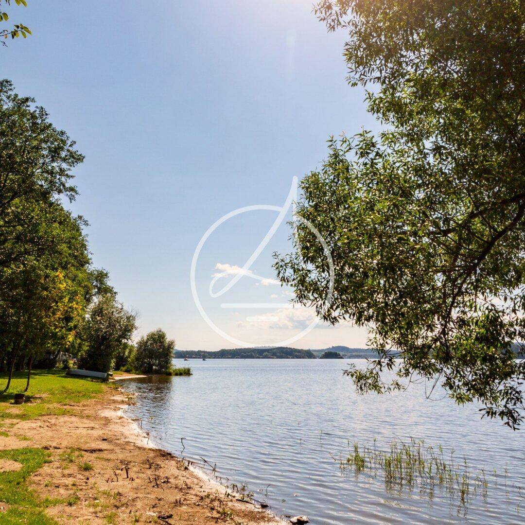 Ruhiges Seeufer mit Bäumen und klarem Wasser an einem sonnigen Tag.