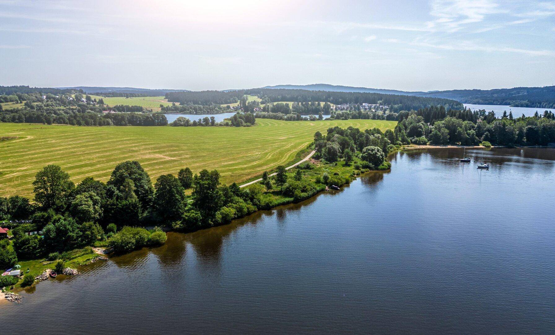 Luftaufnahme einer weiten Seenlandschaft mit grünen Feldern und bewaldeten Hügeln.