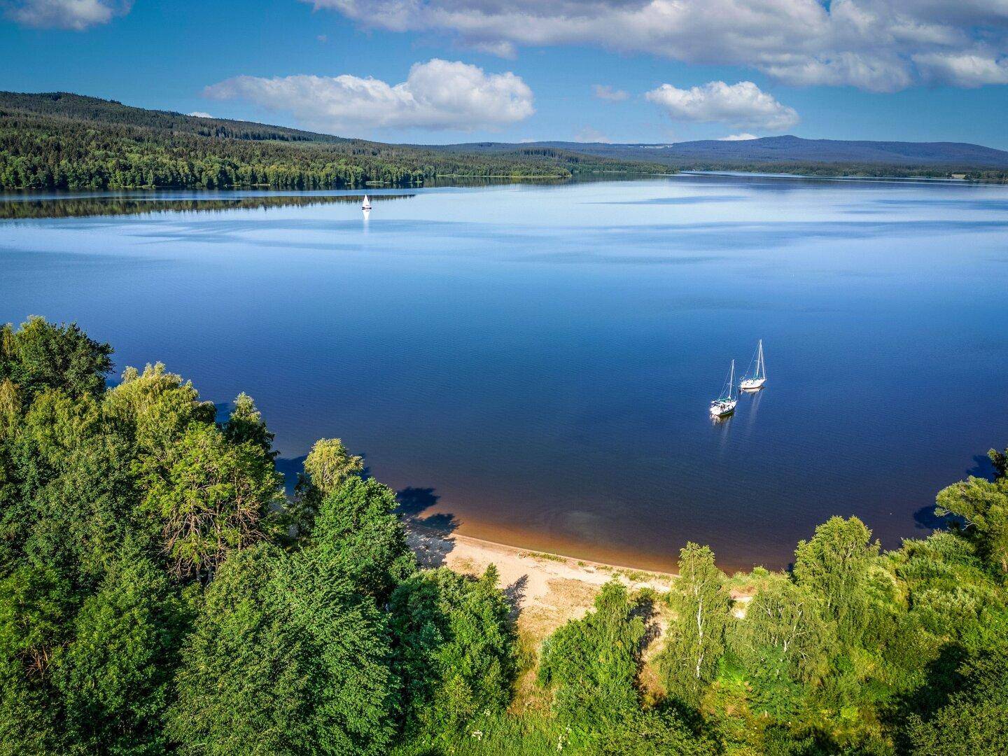 Malerischer See umgeben von Wäldern und Bergen unter einem strahlend blauen Himmel.