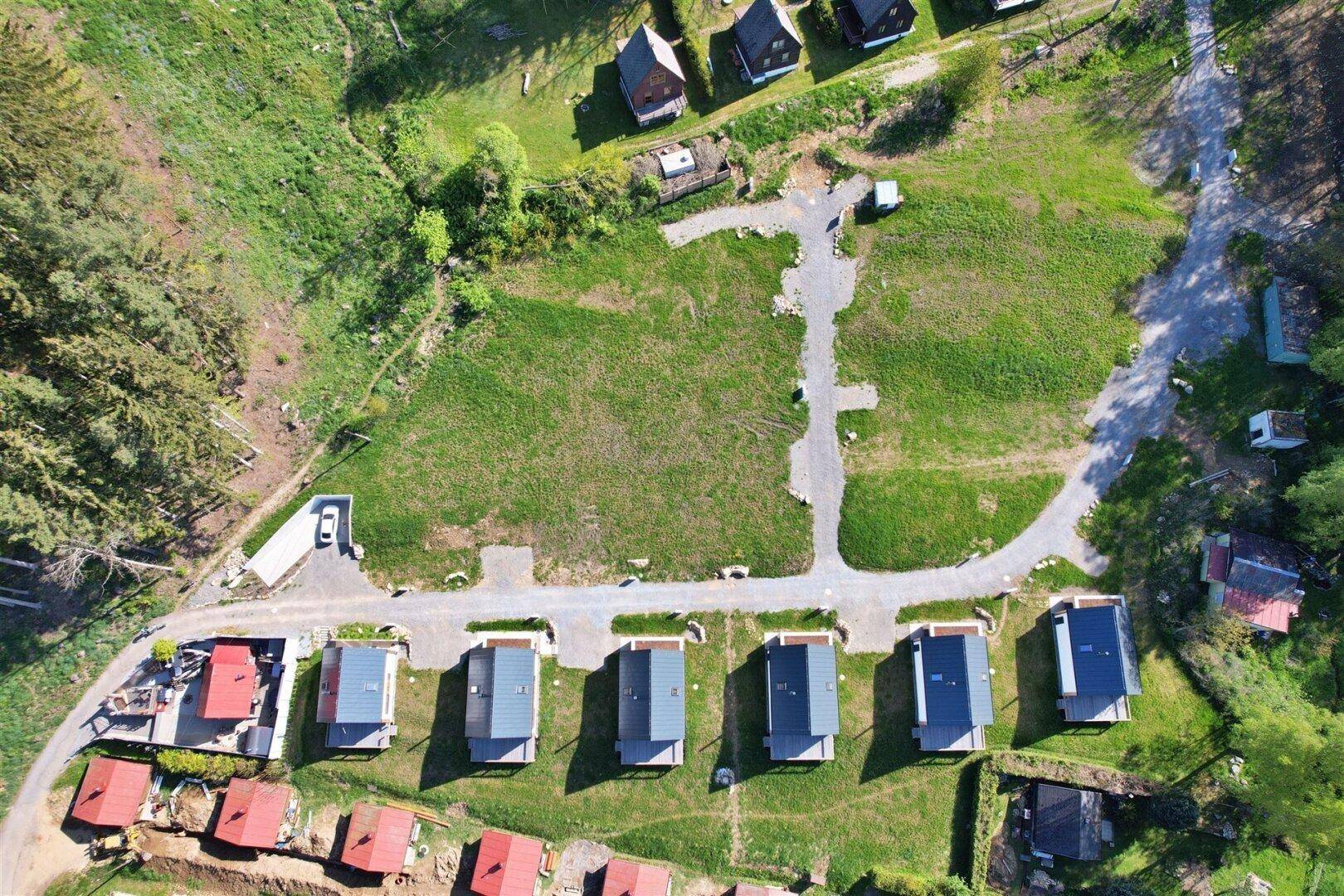 Senkrechte Luftaufnahme einer Reihe moderner Häuser mit grauen Dächern und Holzfassaden in ländlicher Umgebung.