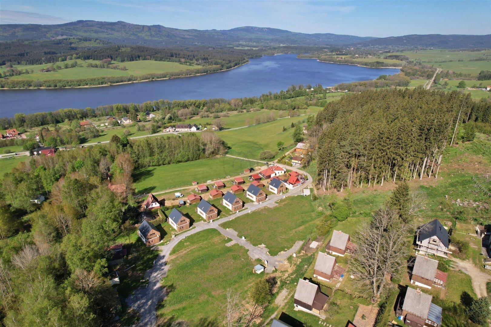 Weitläufige Luftaufnahme einer Wohnsiedlung mit modernen Häusern, umgeben von Natur, See und Wald.