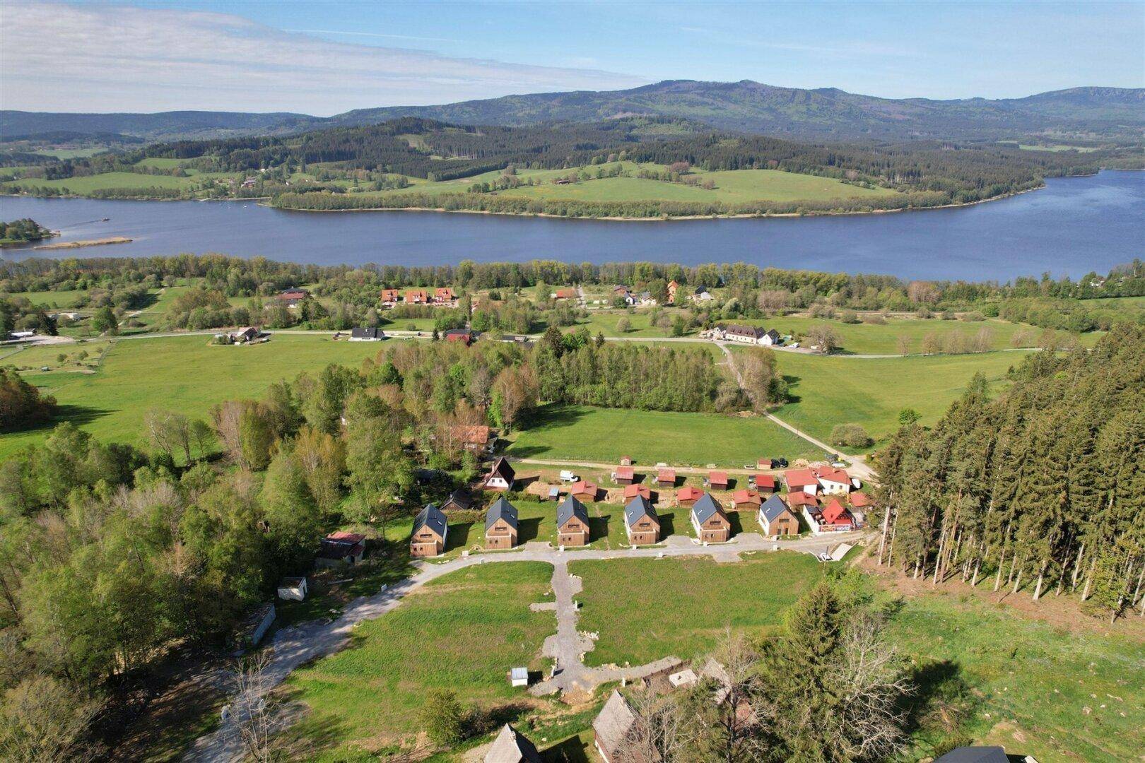Panoramablick aus der Vogelperspektive auf eine Ansammlung von Häusern nahe einem großen See und Waldgebiet.