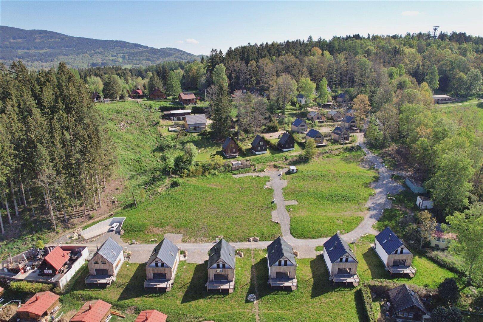Luftaufnahme einer Reihe von modernen Holzhäusern mit Satteldächern, eingebettet in eine grüne Waldlandschaft.