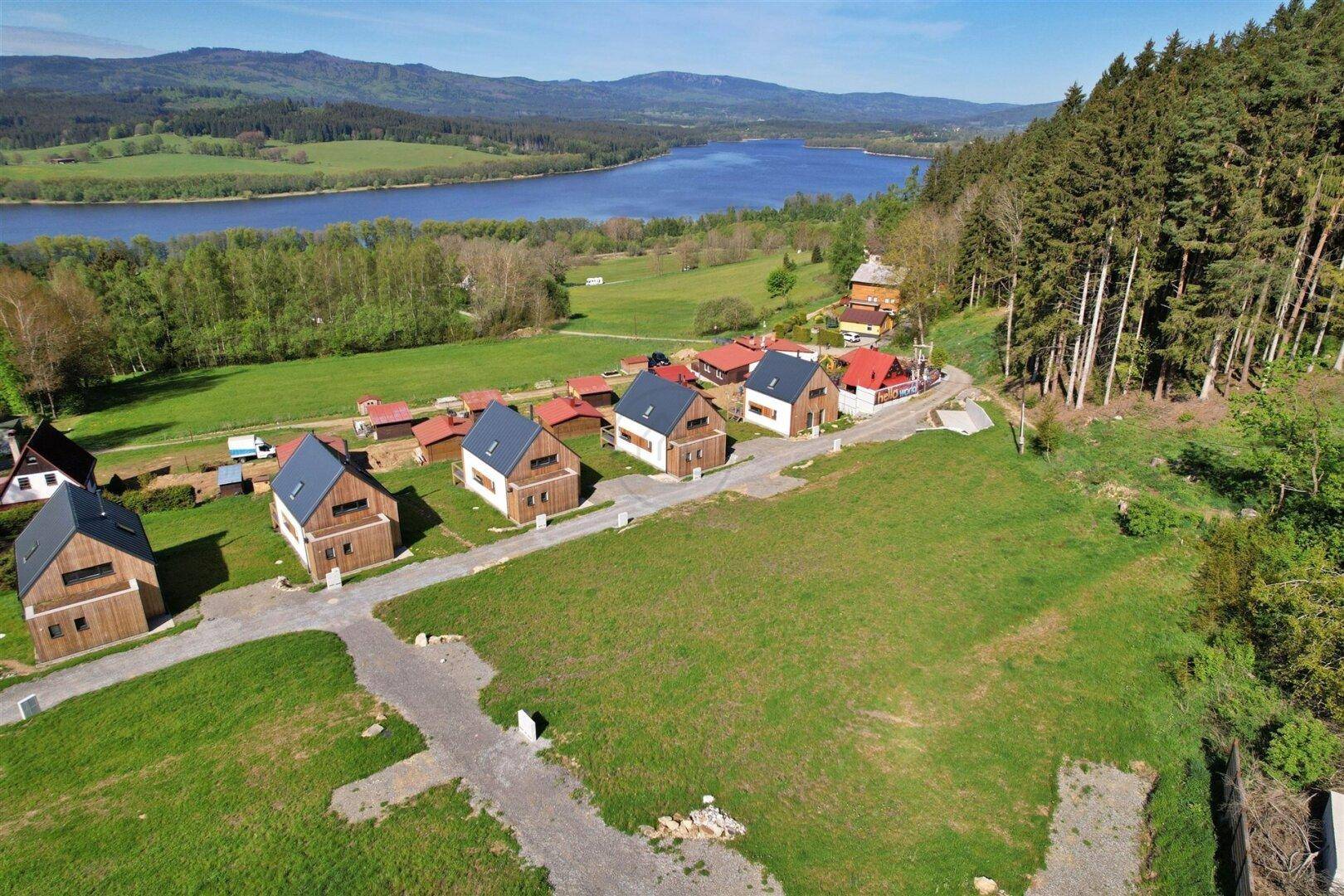Nahaufnahme aus der Luft von modernen Holzhäusern mit dunklen Dächern und einem See im Hintergrund.