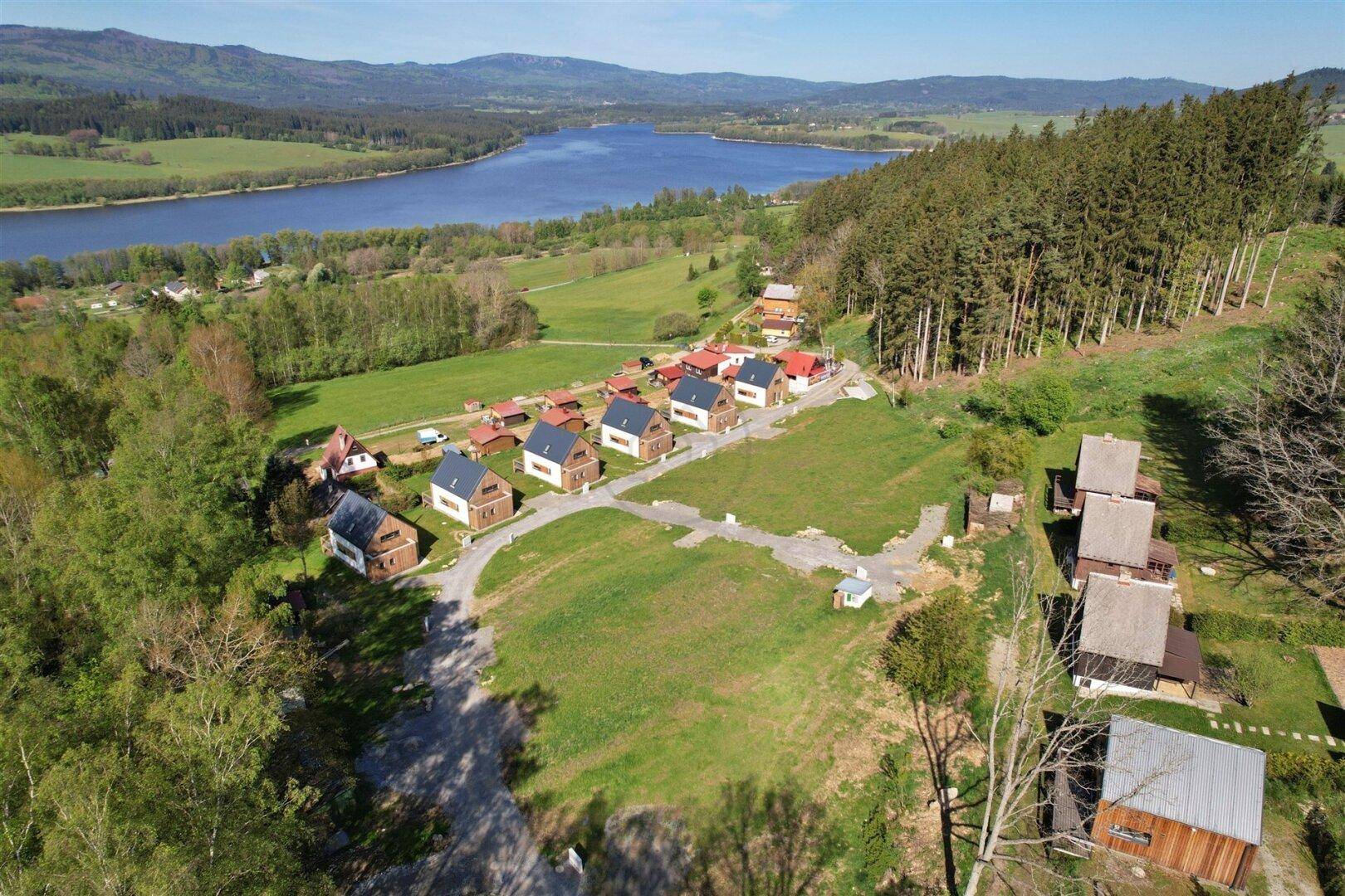 Panoramische Luftaufnahme einer idyllischen Wohnanlage am Waldrand mit Blick auf einen großen See.