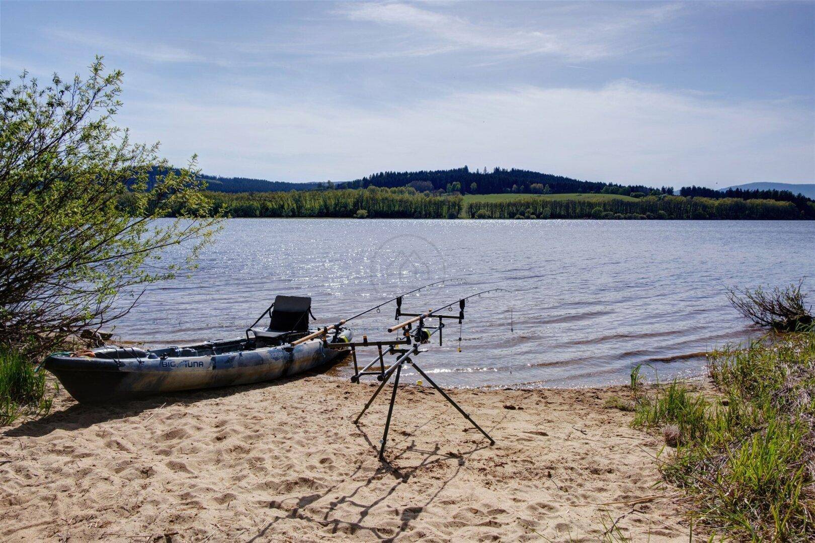 Sandstrand am Seeufer mit einem kleinen Boot und Angelruten, umgeben von grüner Natur.