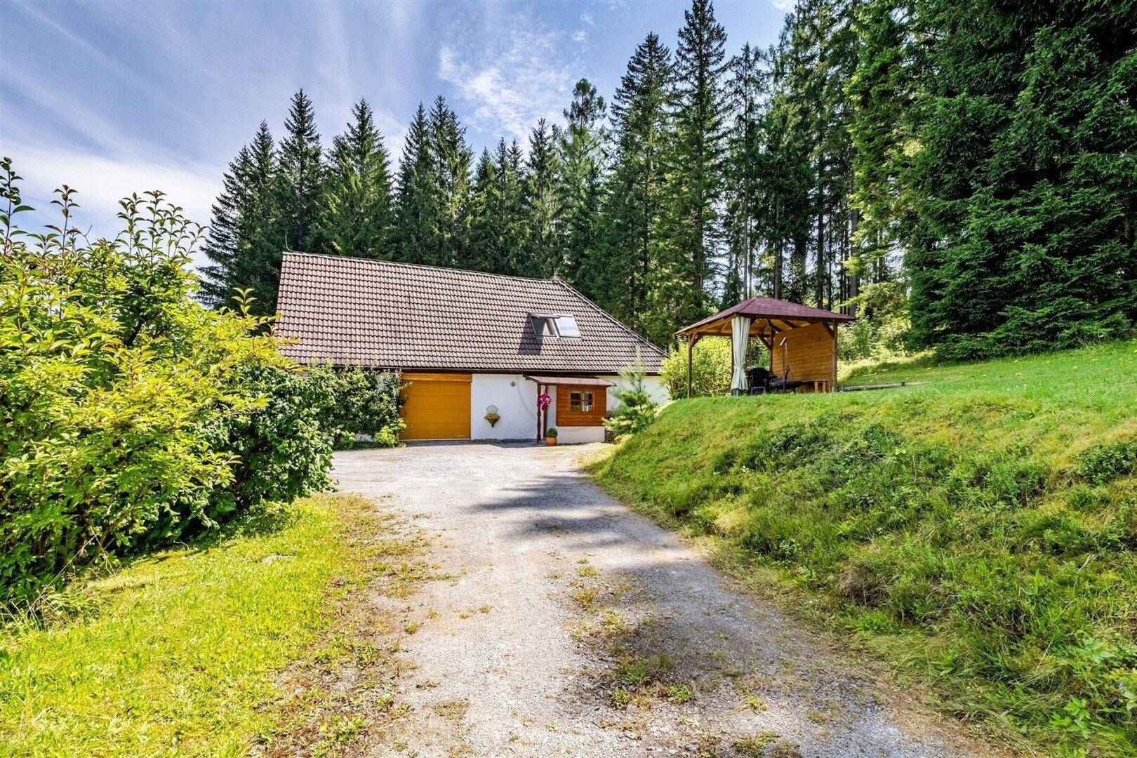 Landhaus mit Zufahrt, umgeben von Bäumen und einem Pavillon im Grünen.
