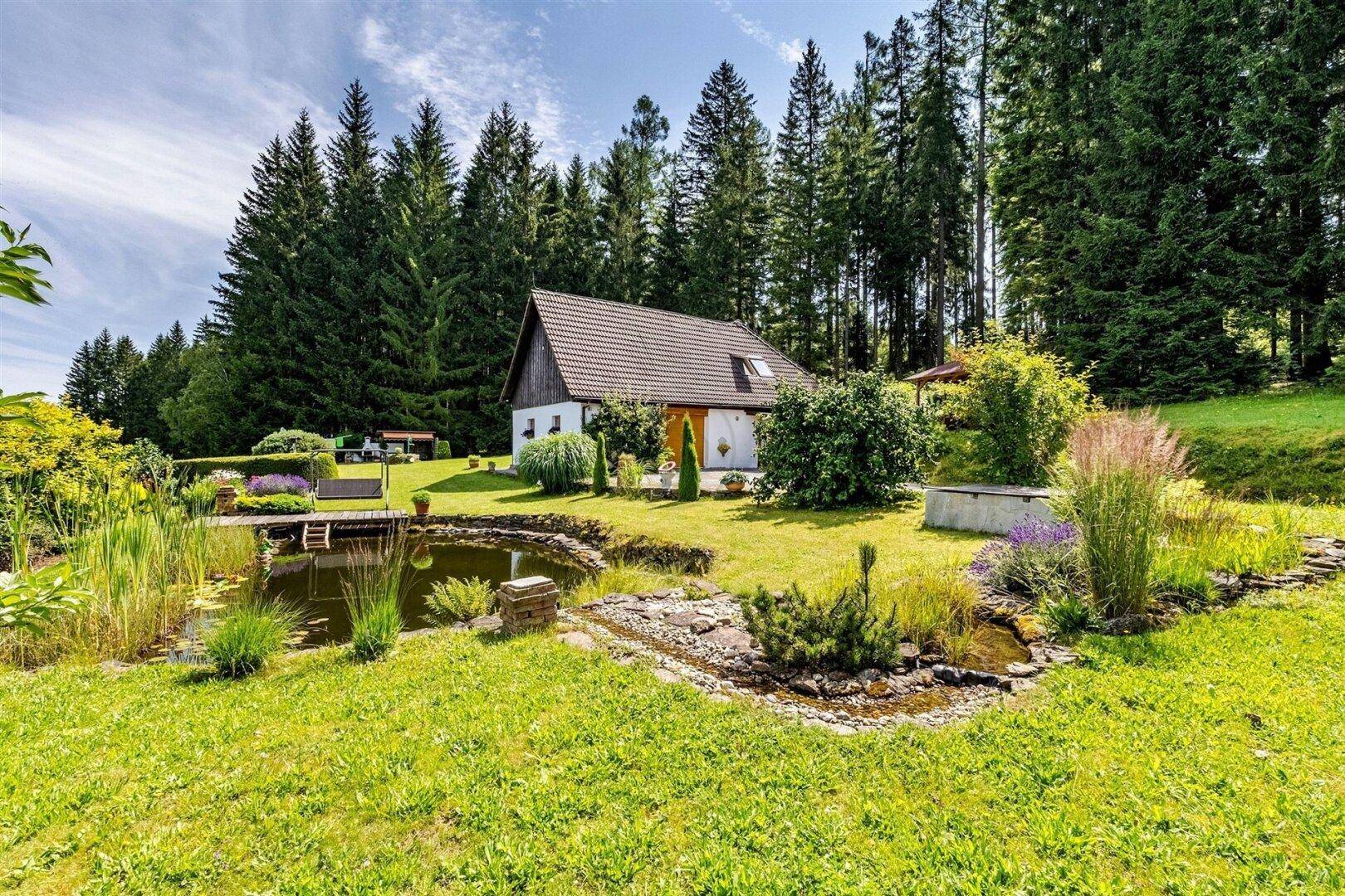 Malerisches Landhaus mit großem Teich und üppiger Bepflanzung, eingebettet in eine grüne Landschaft.