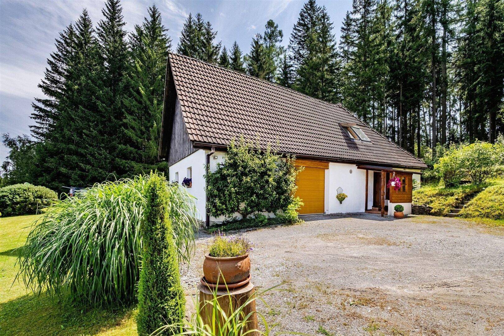 Charmantes Landhaus mit Satteldach und Kiesauffahrt, umgeben von üppiger Natur und hohen Bäumen.