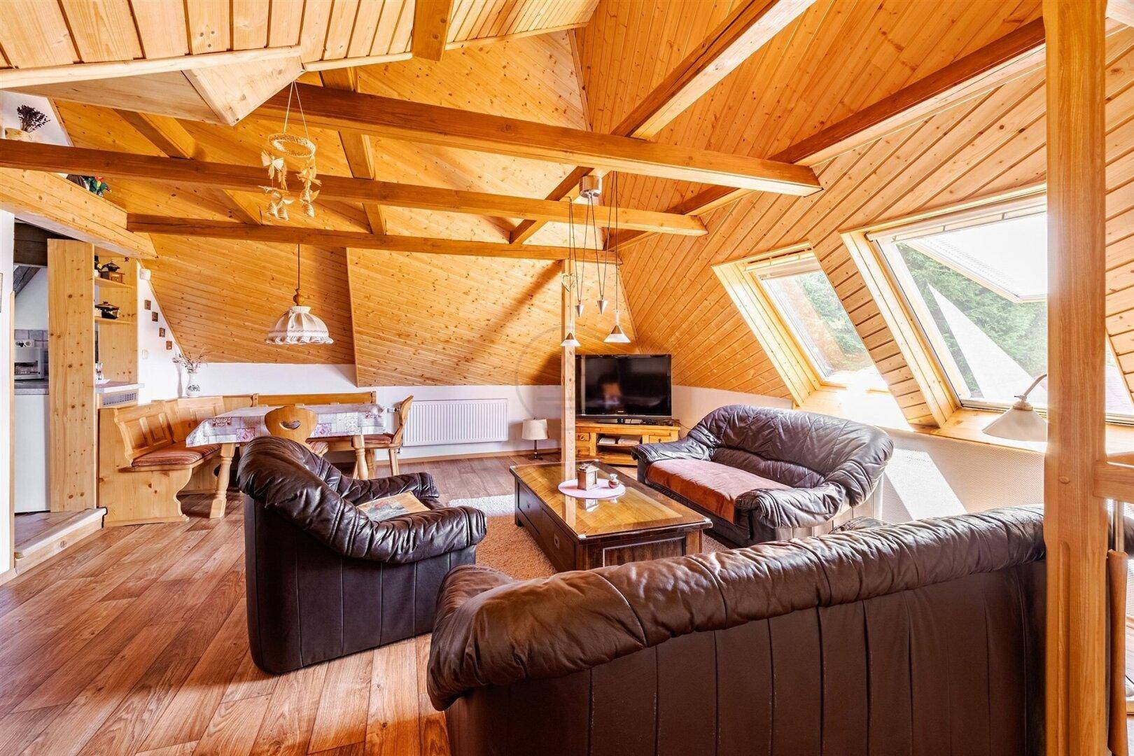 Geräumiger Wohnbereich im Dachgeschoss mit Holzbalken, Ledersofas und Dachfenstern, sehr hell.