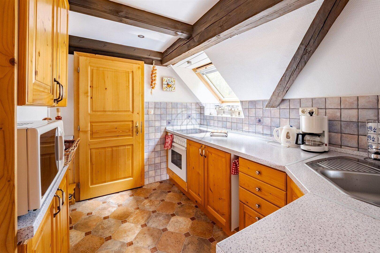 Kleine Küche im Dachgeschoss mit Holzschränken, Fliesenboden und Dachfenster, funktional eingerichtet.