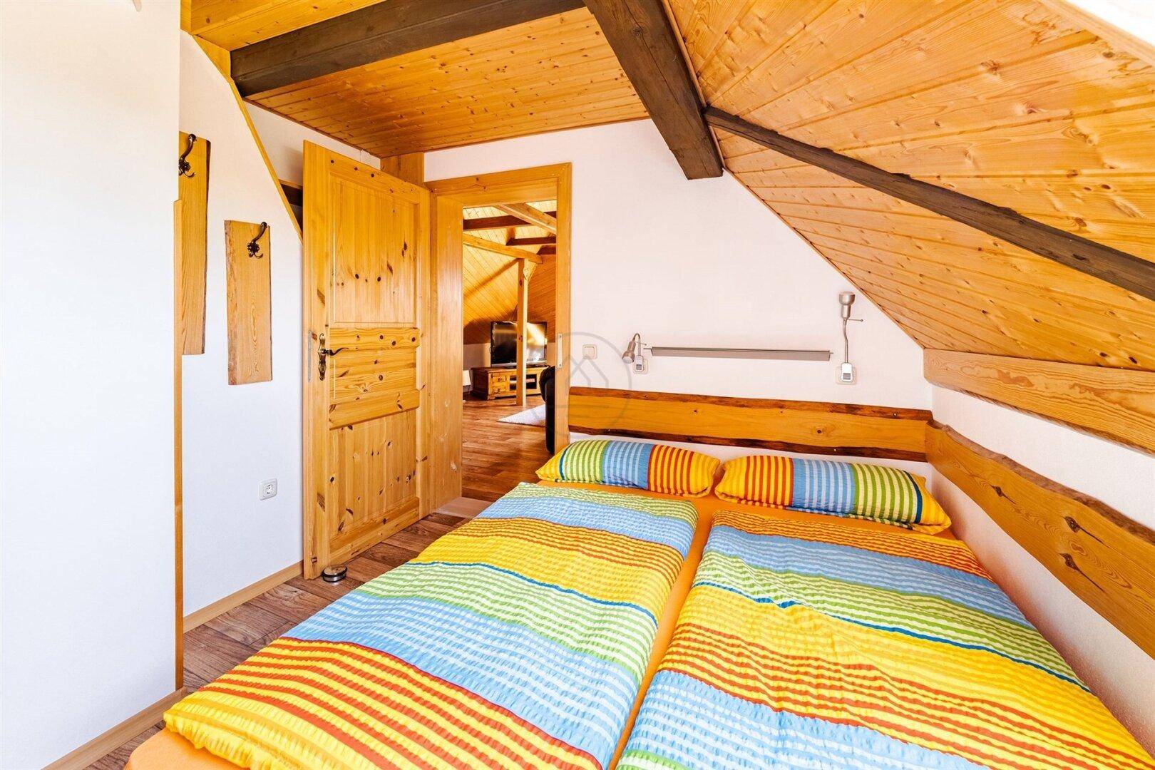 Gemütliches Schlafzimmer im Dachgeschoss mit Holzverkleidung und bunten Betten unter schräger Decke.