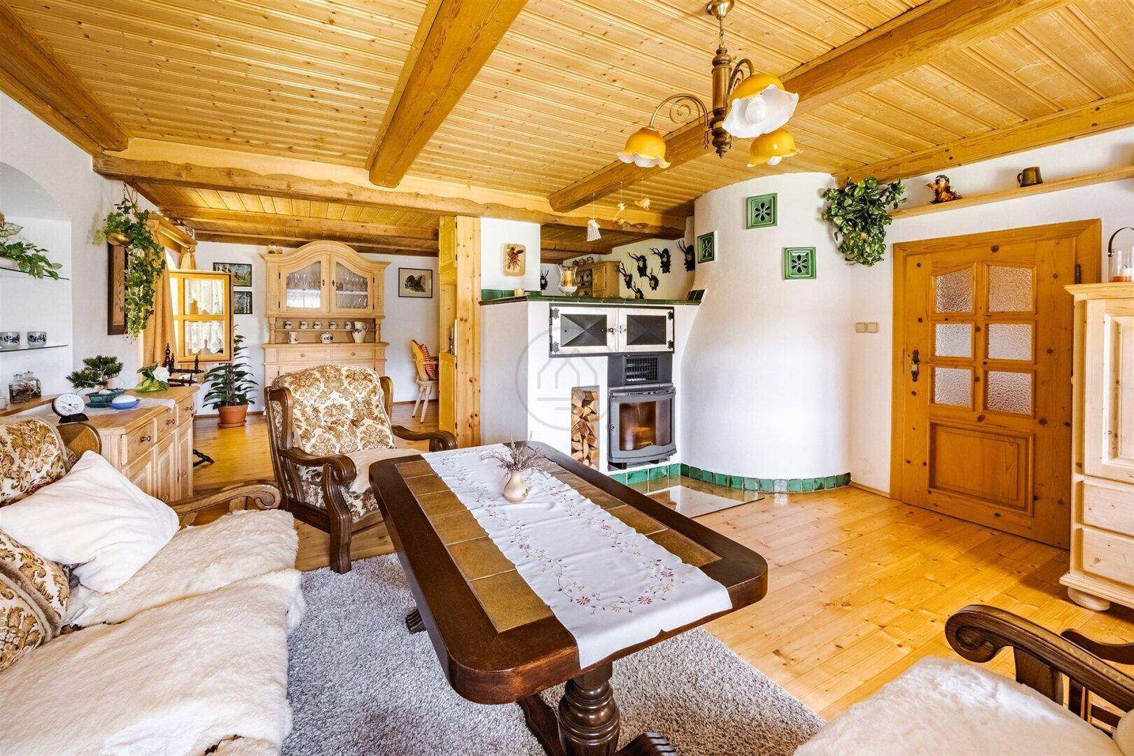Rustikales Wohnzimmer mit Holzboden, Kachelofen und traditionellen Möbeln, strahlt Gemütlichkeit aus.
