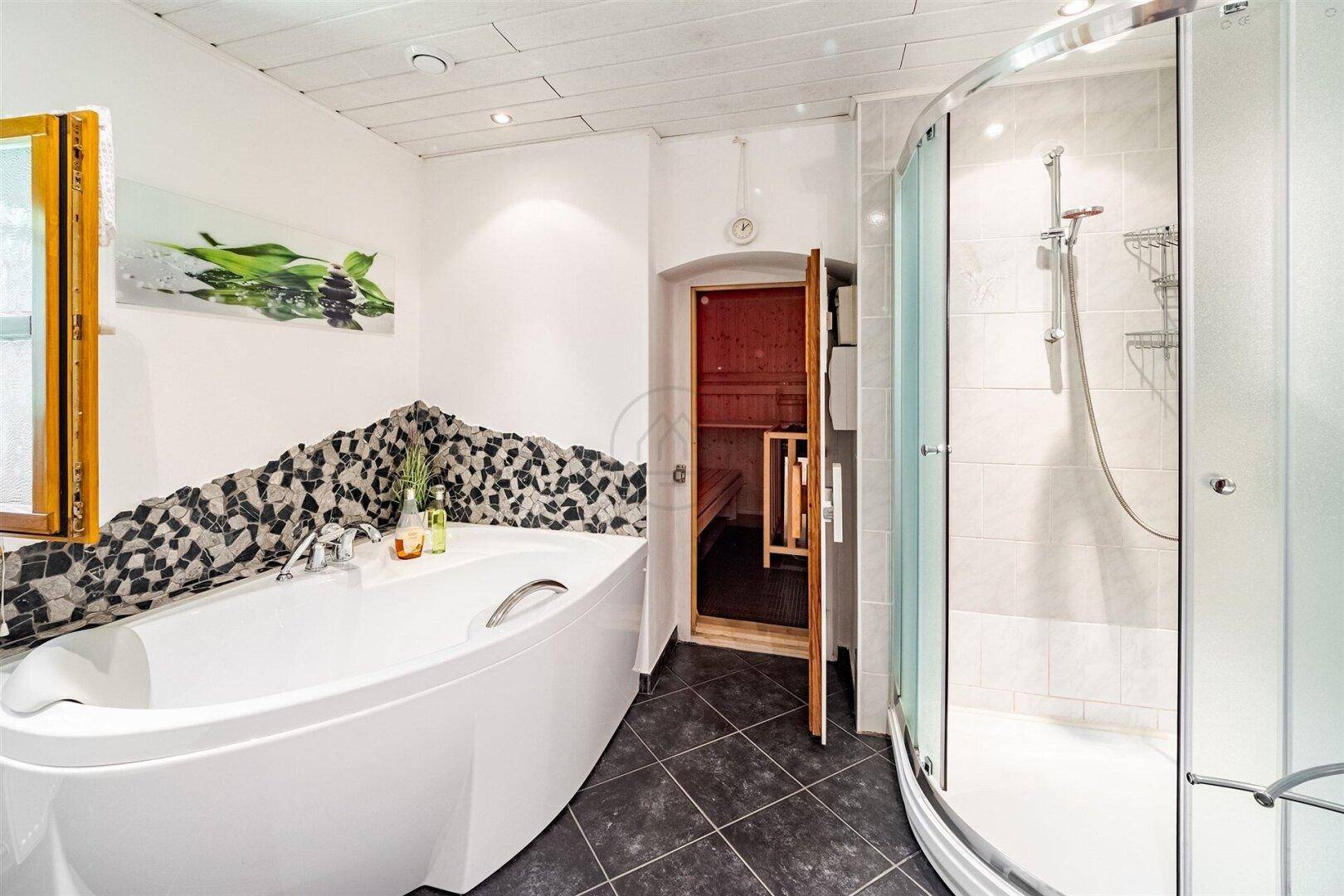 Modernes Badezimmer mit Badewanne, Duschkabine und Zugang zu einer Sauna, bietet Wellness-Komfort.