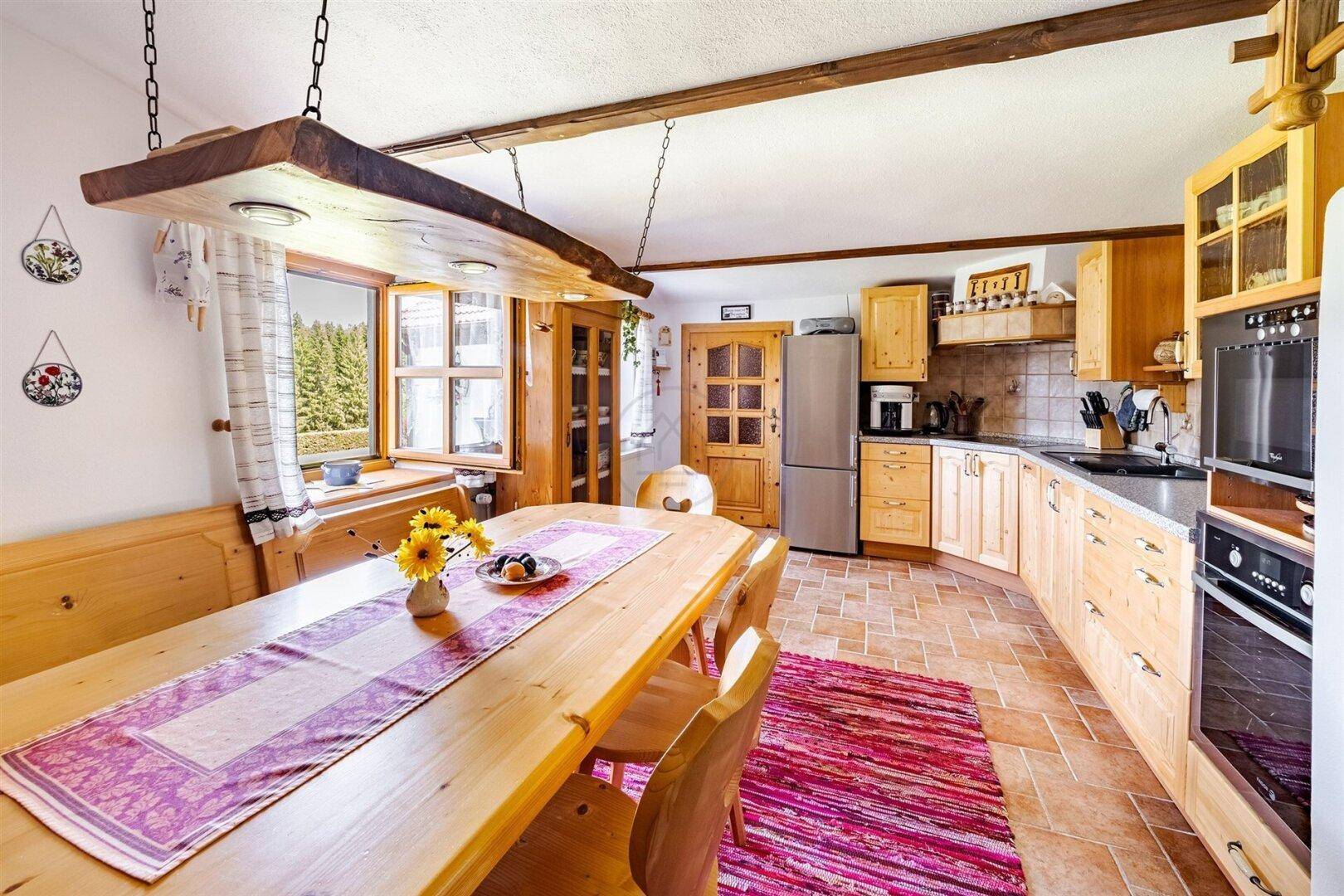 Geräumige Wohnküche im Landhausstil mit Holzeinbauten, Essbereich und Blick ins Grüne.
