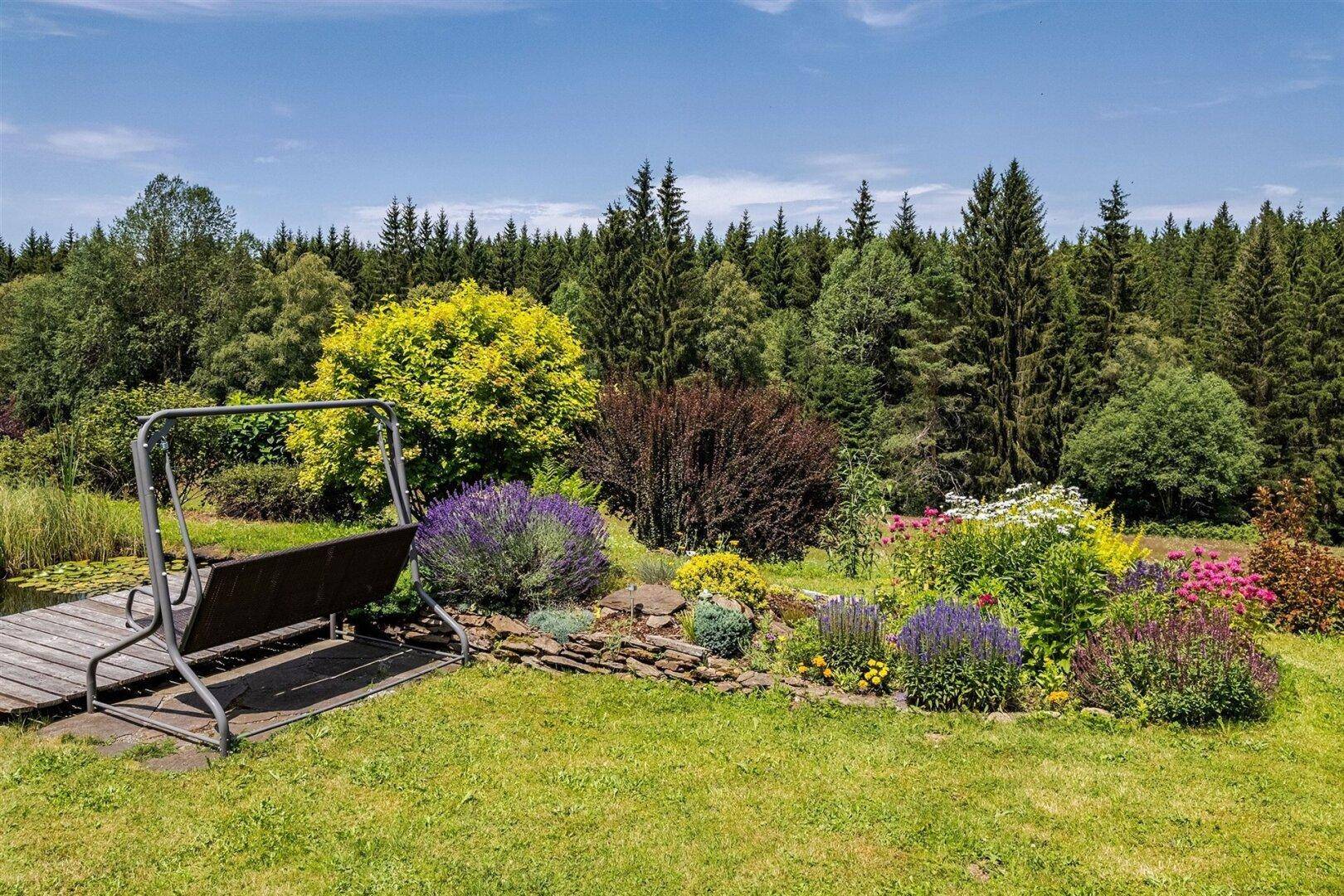 Gepflegter Gartenbereich mit Schaukel, bunten Blumenbeeten und weitem Blick auf den Wald.