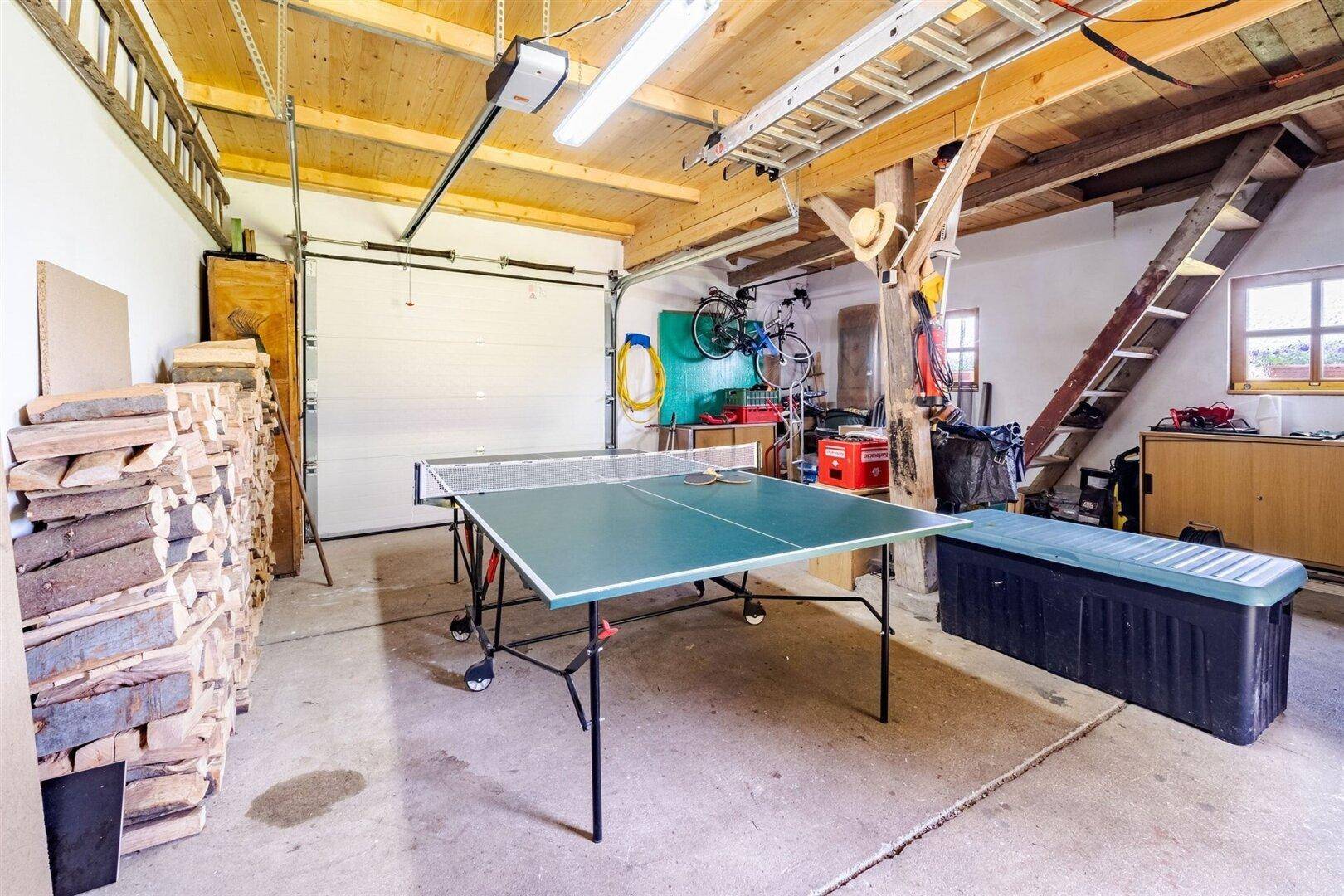 Geräumige Garage mit Tischtennisplatte, Holzstapel und Stauraum, ideal für Freizeitaktivitäten.