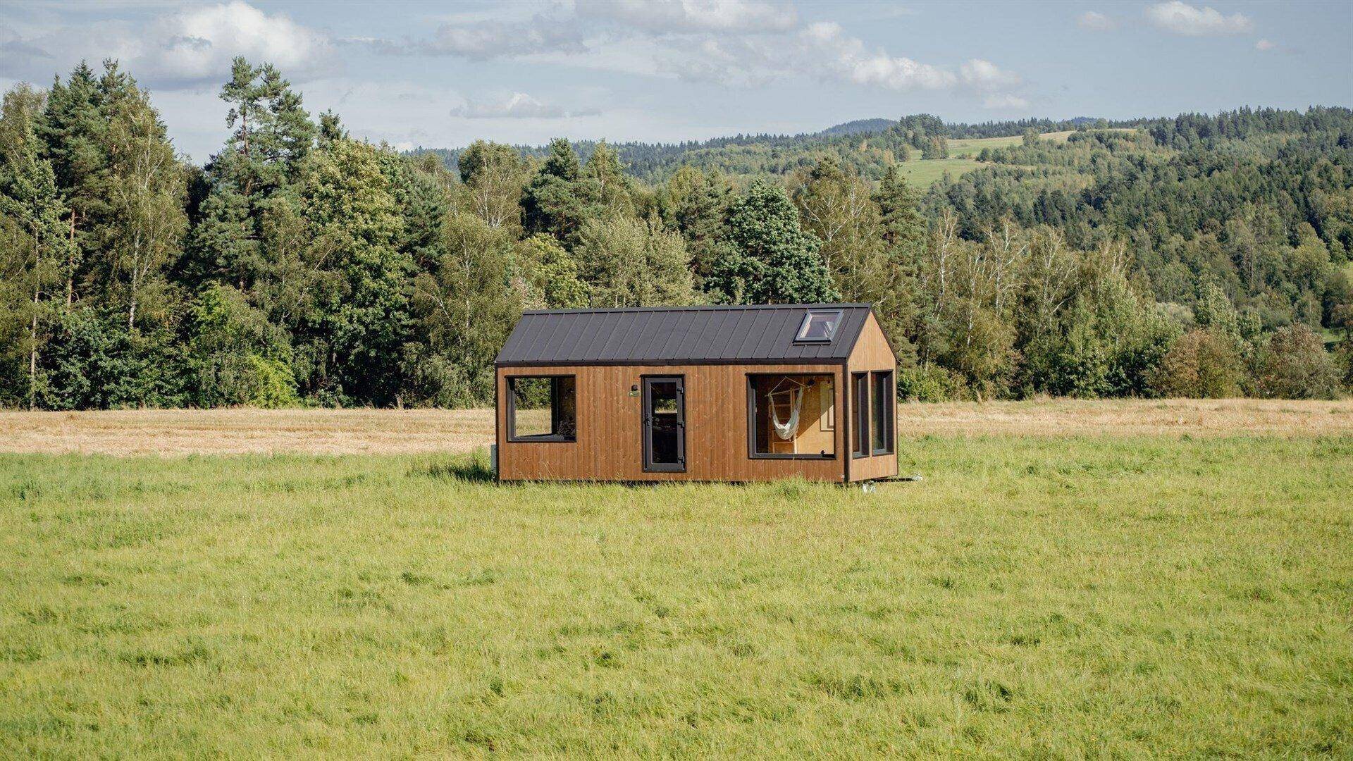 Modernes Tiny House mit Holzfassade und großen Fenstern, umgeben von grüner Natur.