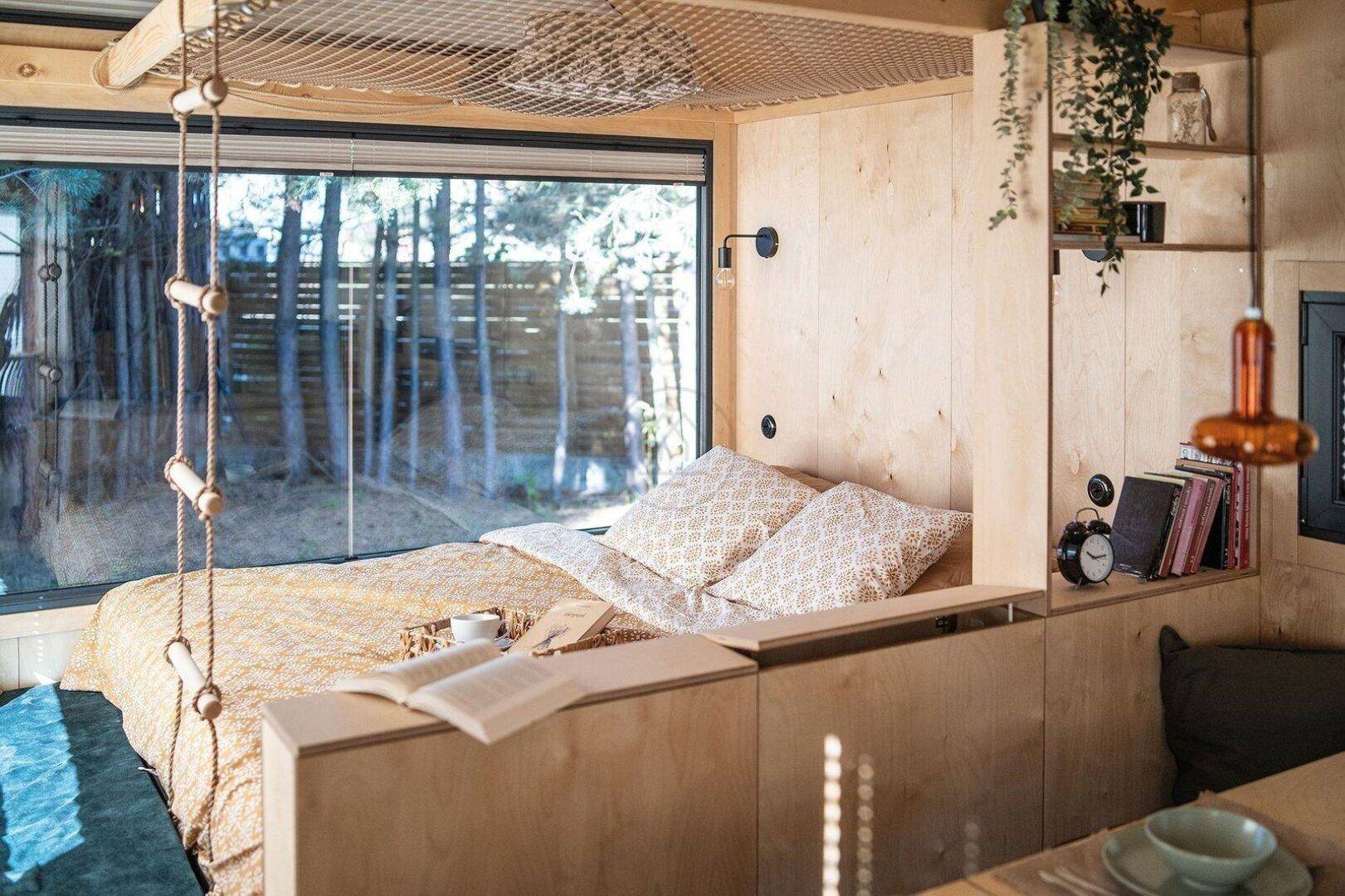 Helles Schlafzimmer mit Holzwänden, großem Fenster und Blick auf die umgebende Waldlandschaft.