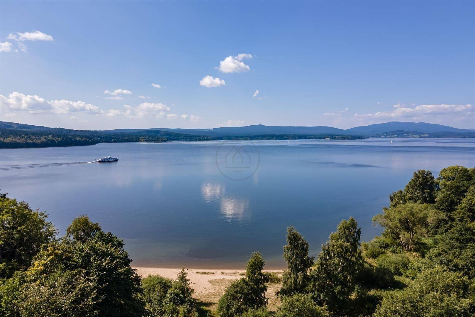 Luftaufnahme des großen Sees mit bewaldeten Ufern und einem Schiff auf dem Wasser.
