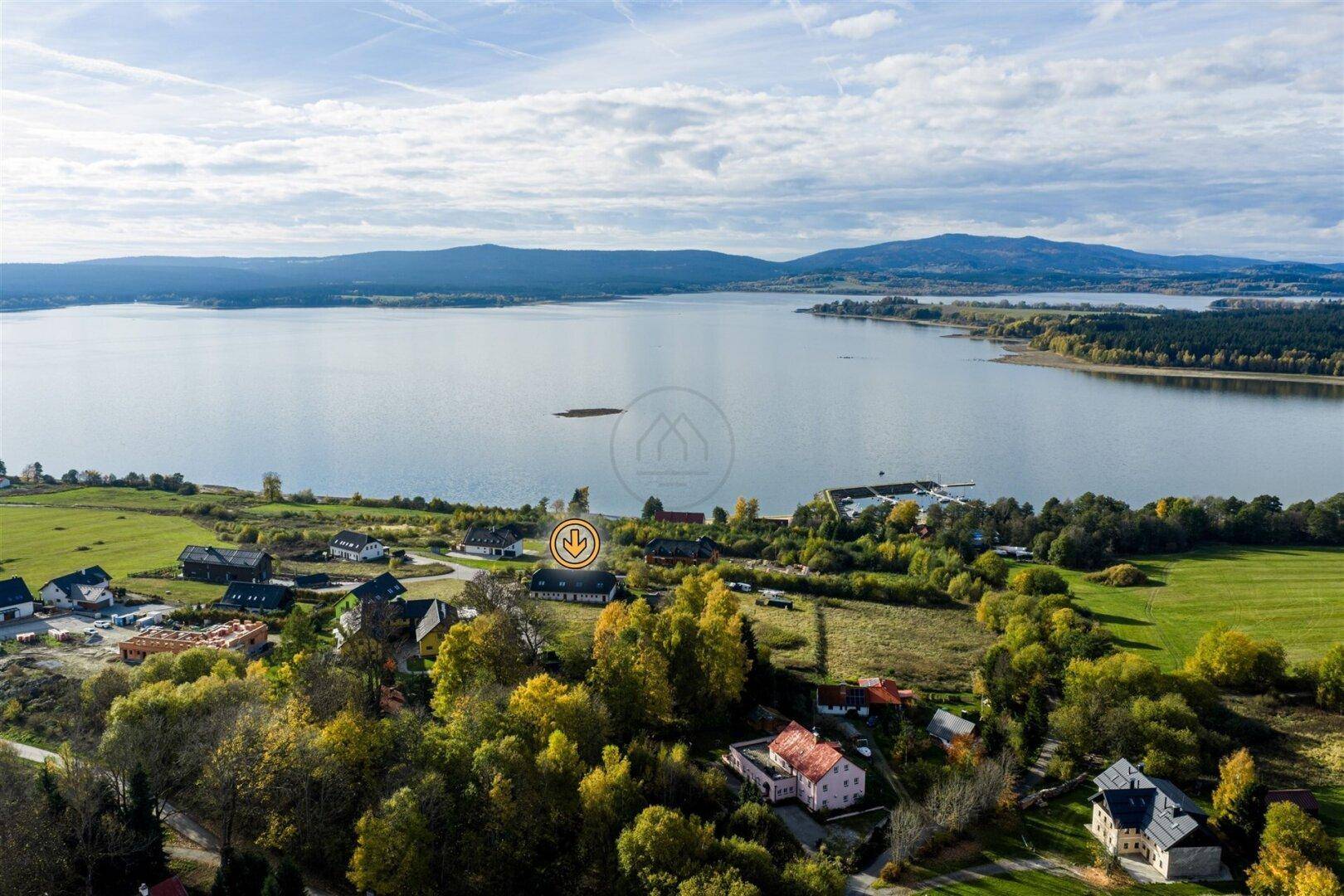 Luftaufnahme der Wohnsiedlung am Seeufer mit Herbstbäumen und Bergen im Hintergrund.