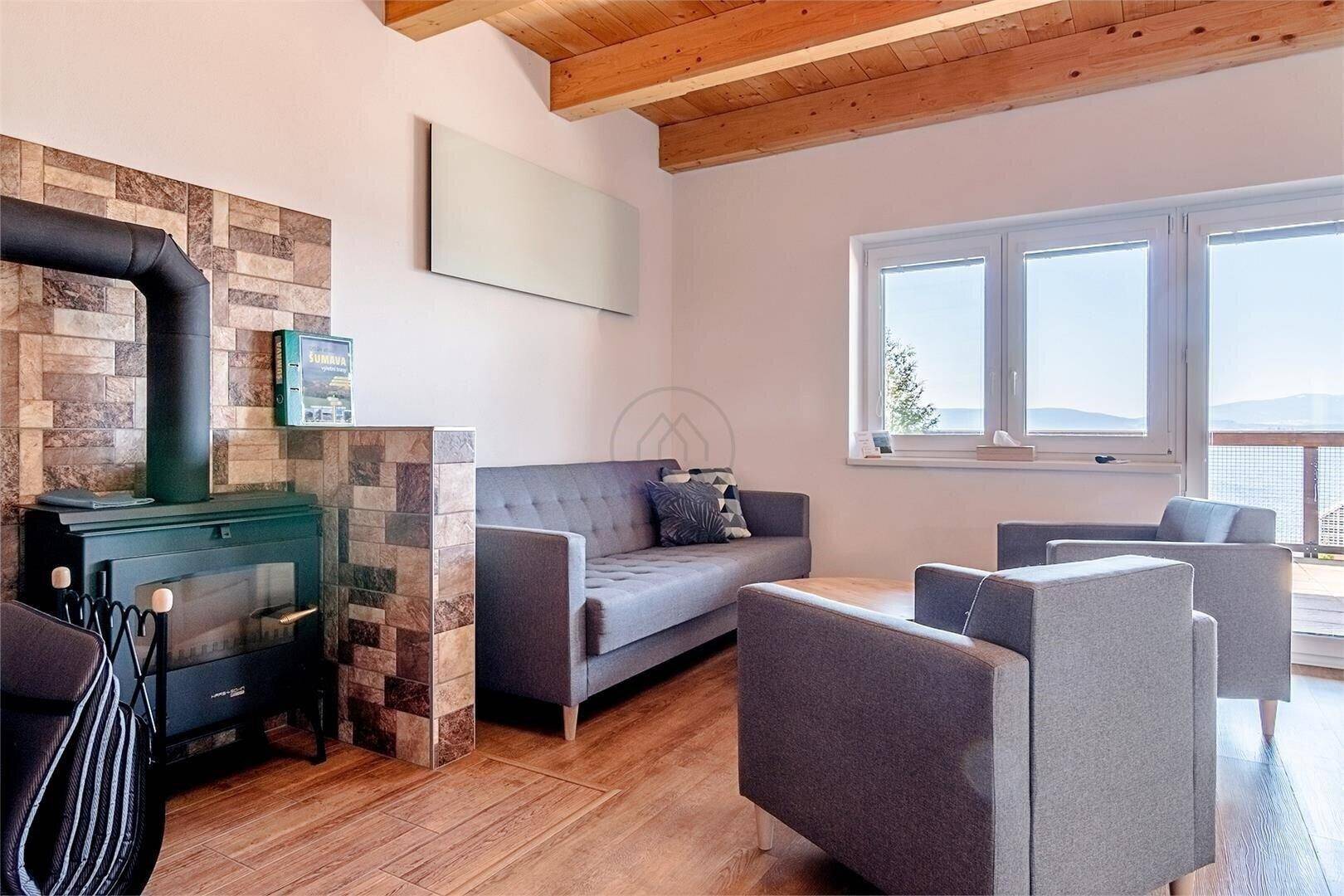 Gemütliches Wohnzimmer mit Holzbalkendecke, Kaminofen und großen Fenstern.