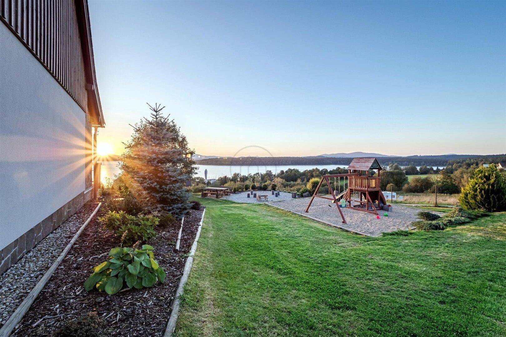 Spielplatz auf einer großen Rasenfläche mit Blick auf den See bei Sonnenuntergang.