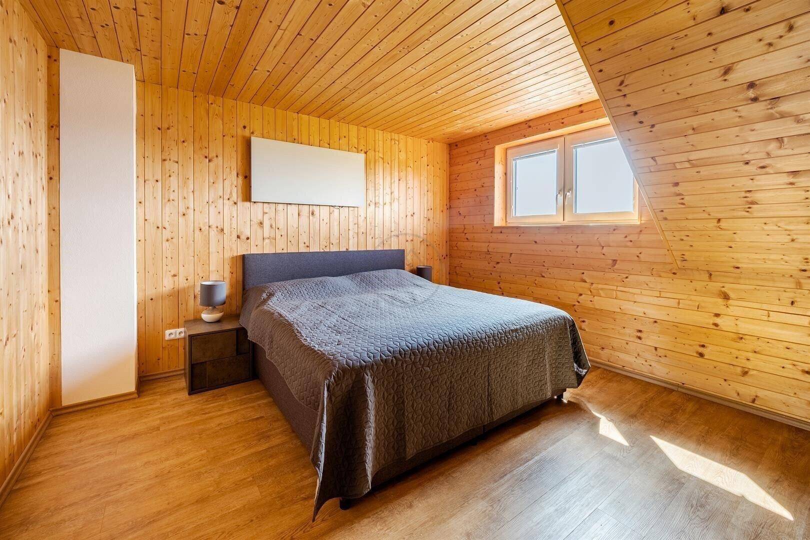 Gemütliches Schlafzimmer mit Holzwänden, Holzboden und Dachschräge.