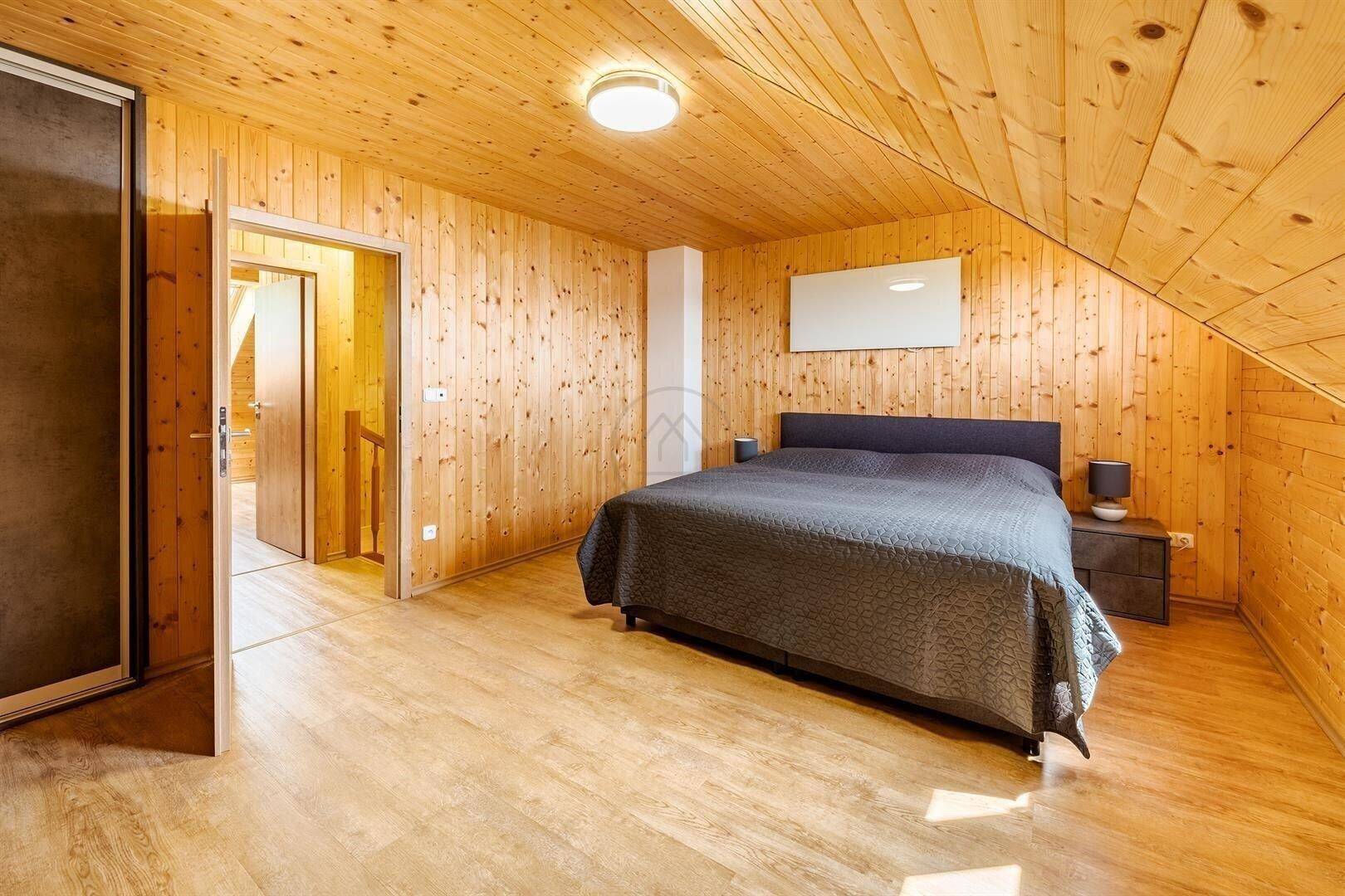 Schlafzimmer im Dachgeschoss mit viel Holz, Laminatboden und Zugang zu weiteren Räumen.