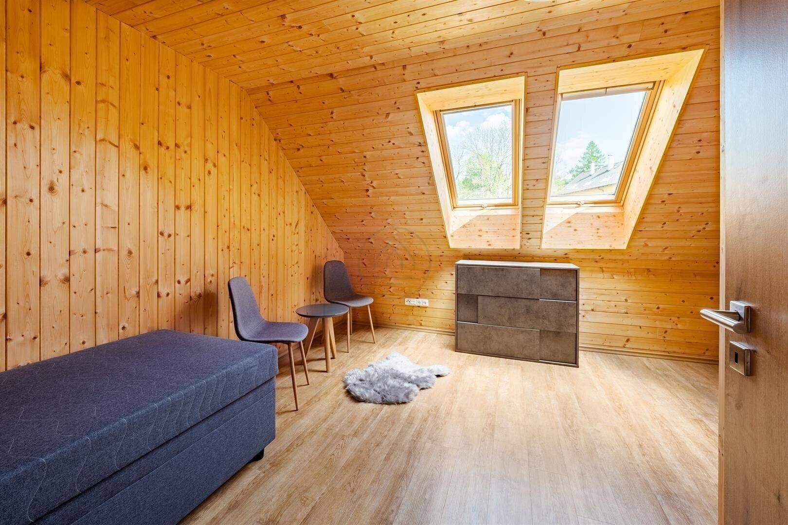Helles Zimmer mit Holzwänden, Dachfenstern und einfacher Einrichtung.