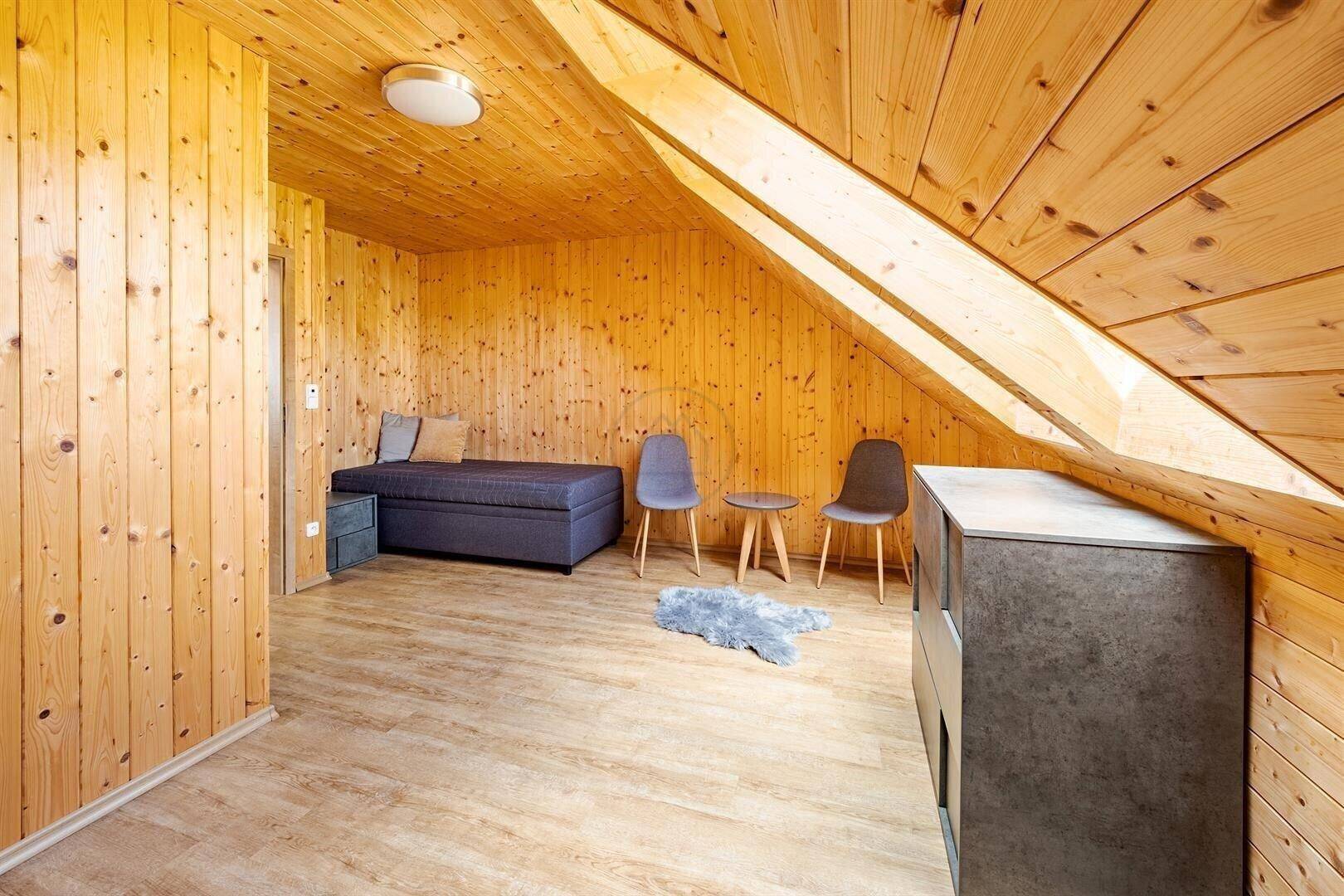 Zimmer mit Holzausstattung, Dachschräge und viel natürlichem Licht durch die Fenster.