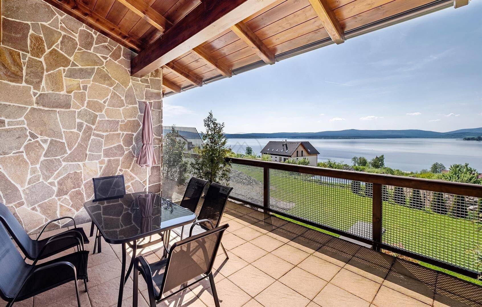 Große überdachte Terrasse mit Sitzgelegenheiten und weitem Blick auf den See.