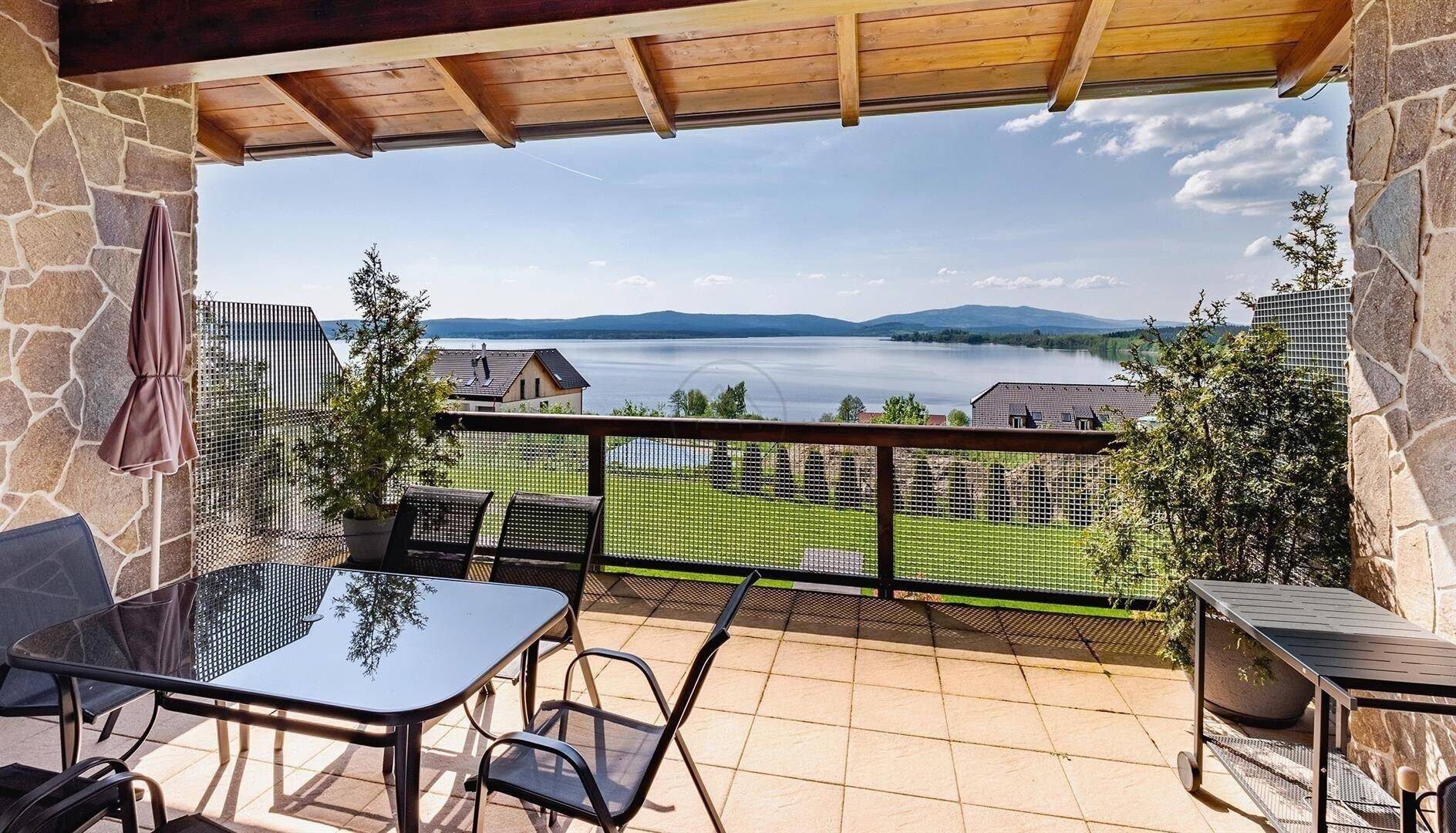 Geräumige Terrasse mit Steinfassade, Esstisch und Panoramablick auf den See und die Landschaft.
